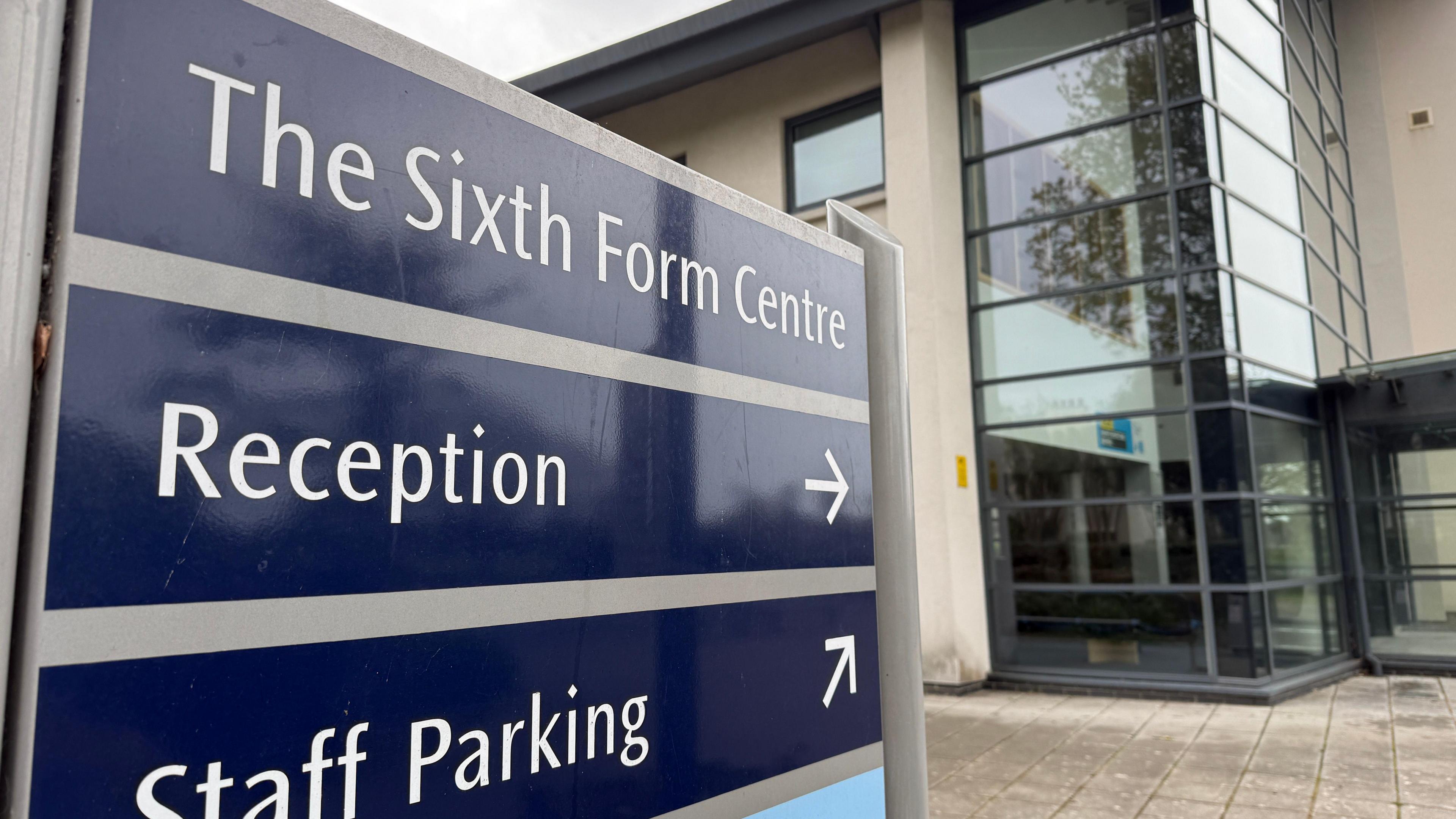 A sign which says The Sixth Form Centre at the top, reception with an arrow pointing towards a building in the background and staff parking, with an arrow pointing around the building.