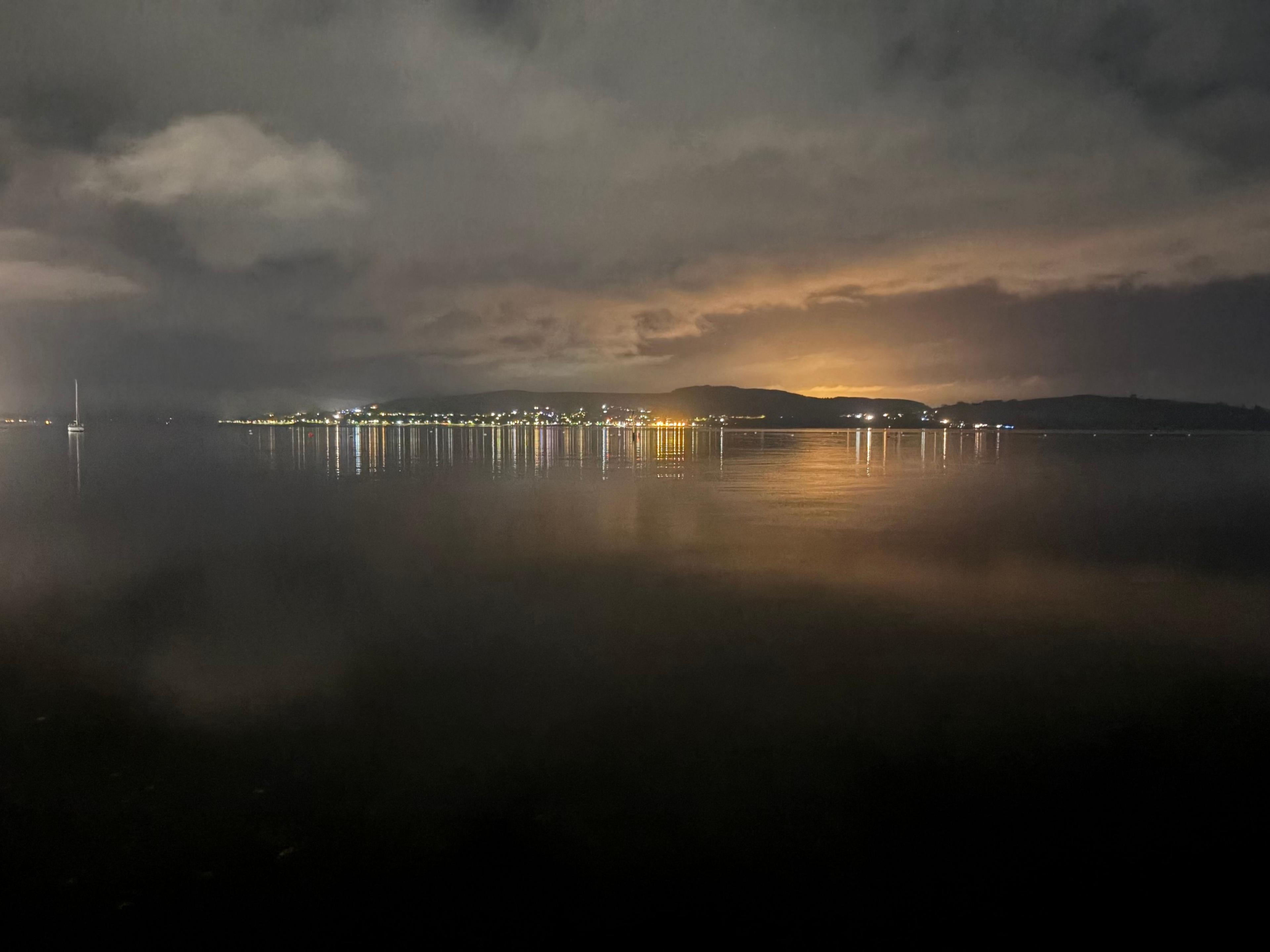 A misty view across a river, with lights from the other side of the bay lit up in the distance