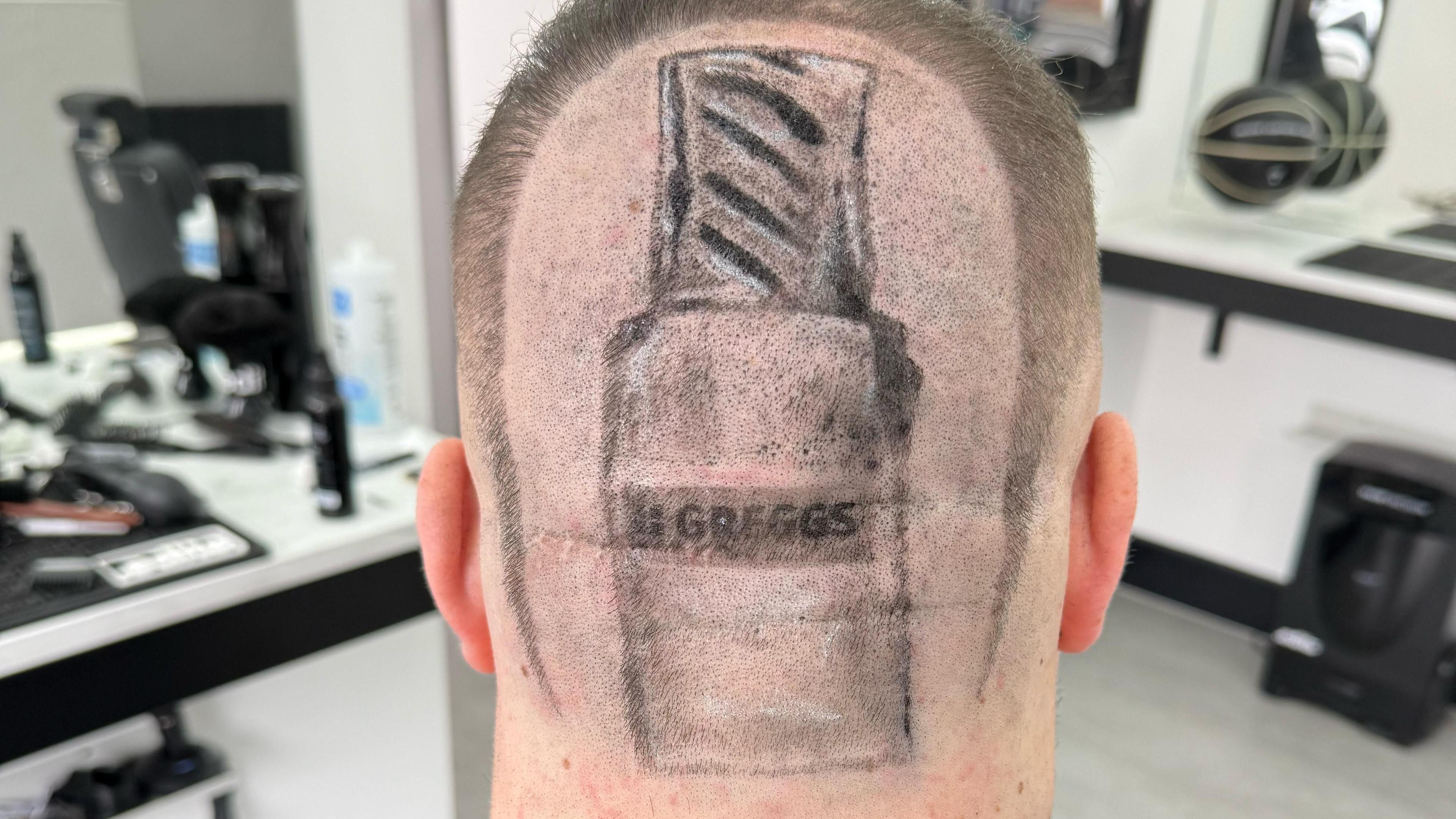 The back of a head with a sausage roll in a Greggs packet shaved into the middle.