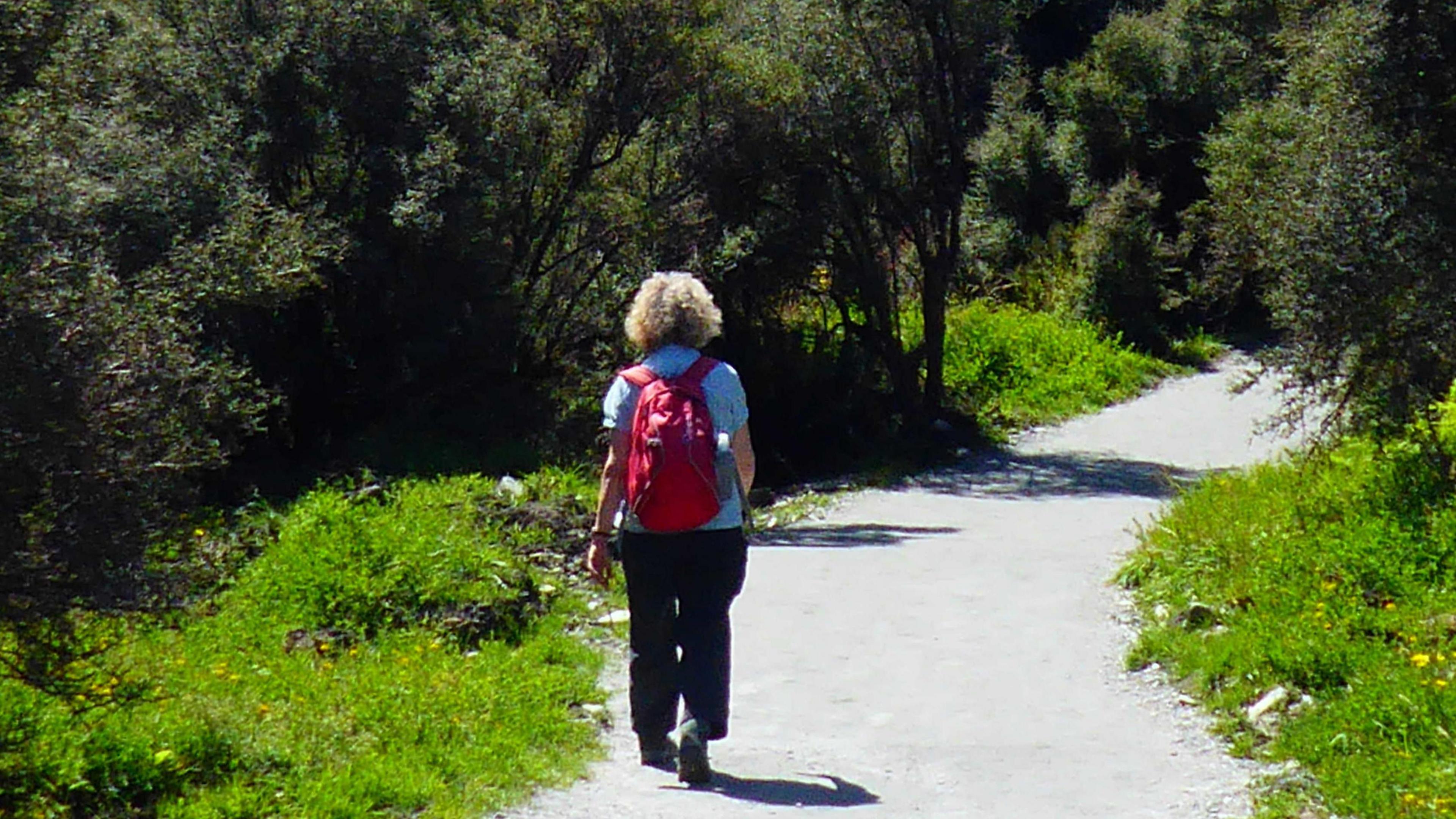 Alison on a walking trail with her back to the camera she is wearing a red backpack