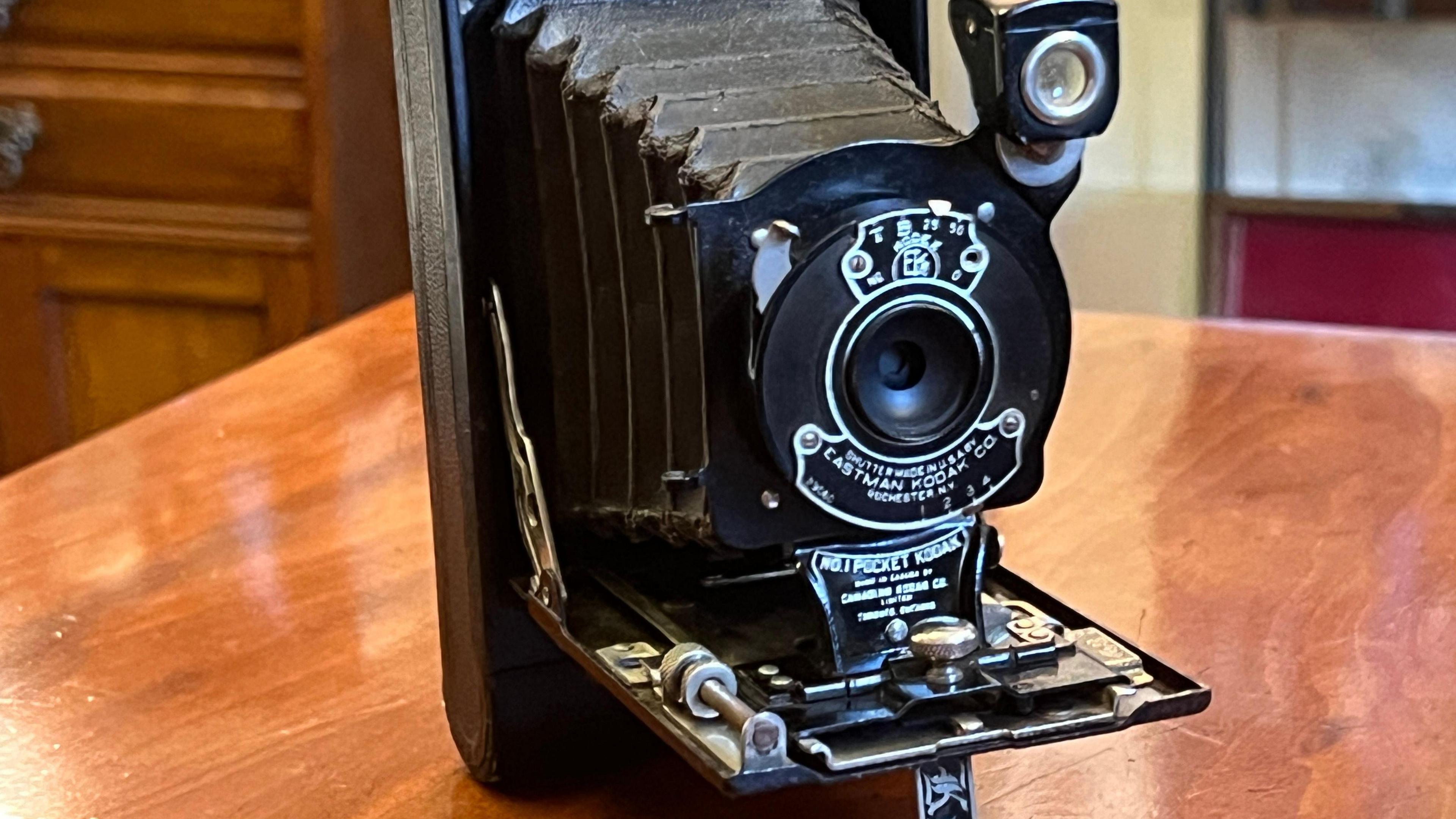 The black Kodak sits on a wooden table with its lens mechanism extended.