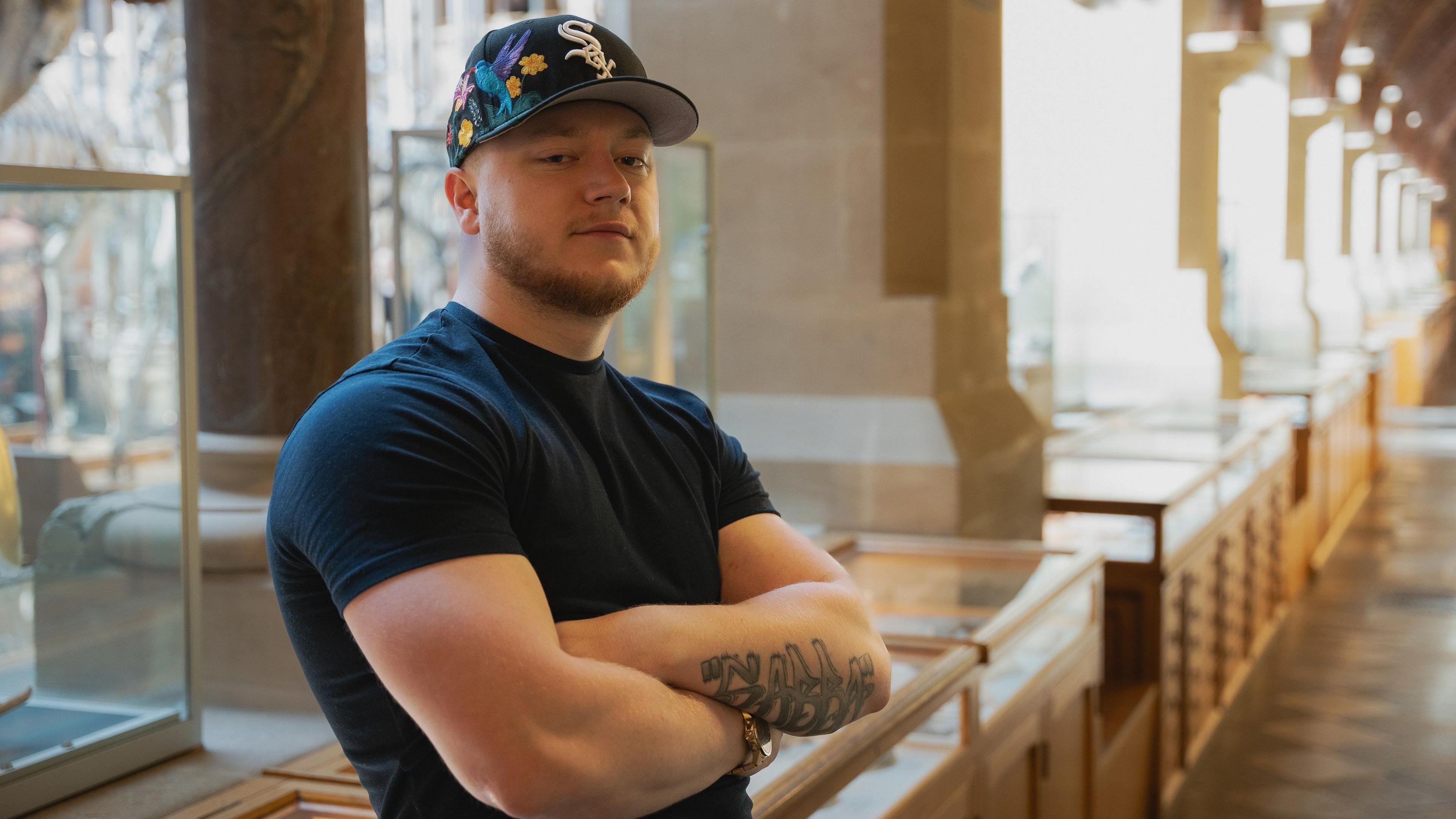 Samuel Mansell stood with a cap on and his arms folded, looking at the camera