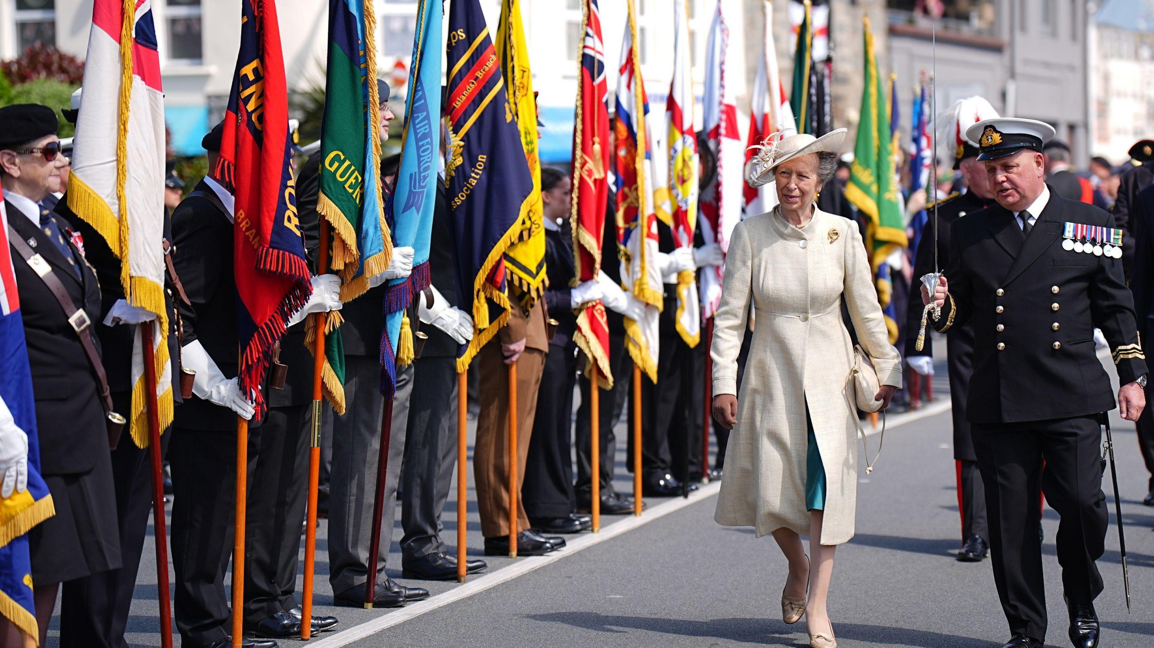 The Princess Royal inspecting a guard of honour during a visit to St Peter Port. She is walking on a road next to a man in a black suit.