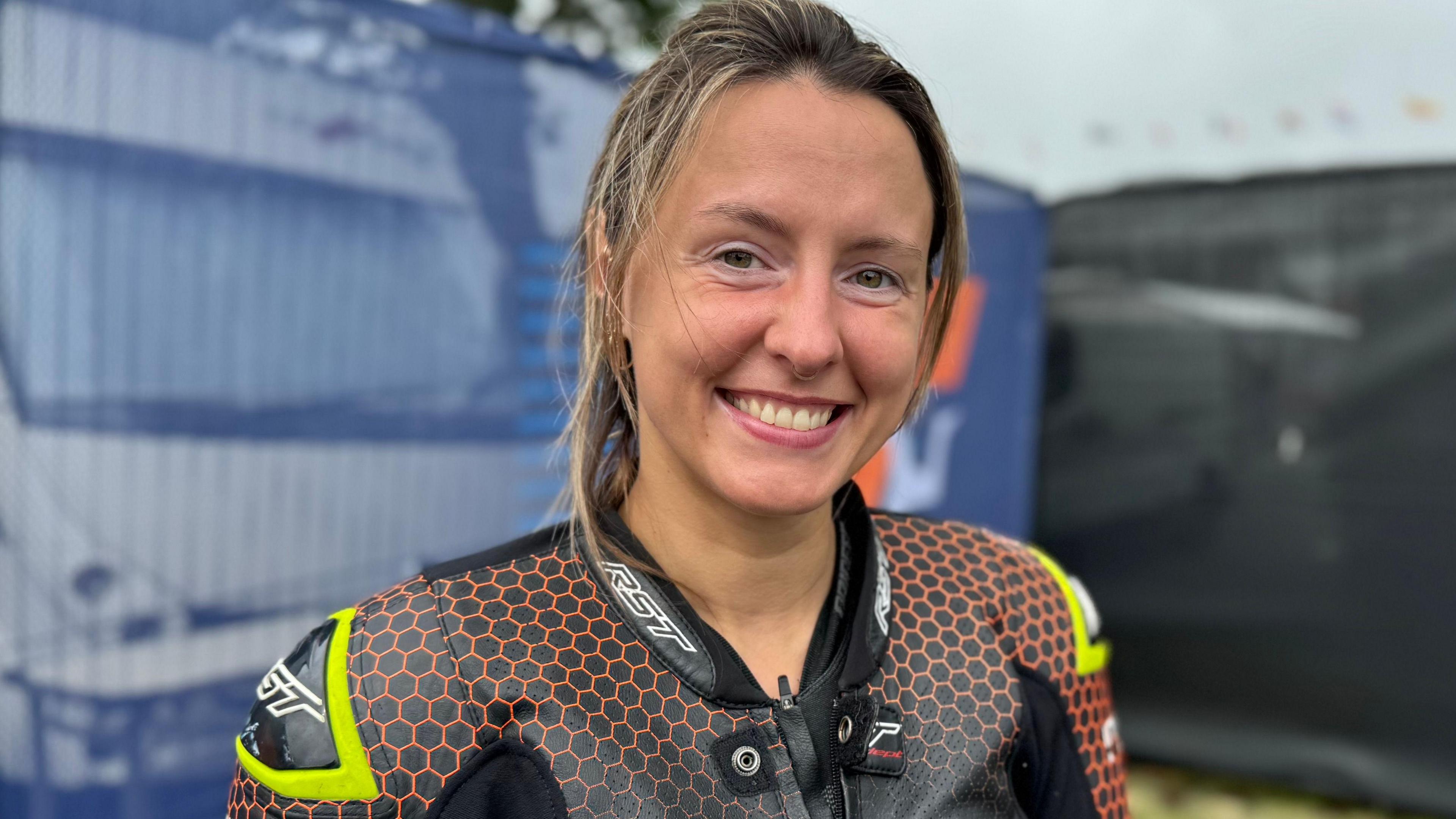 Ola Bolkowska wears black and orange bike leathers. She has dark hair with blonde highlights, which is tied back.