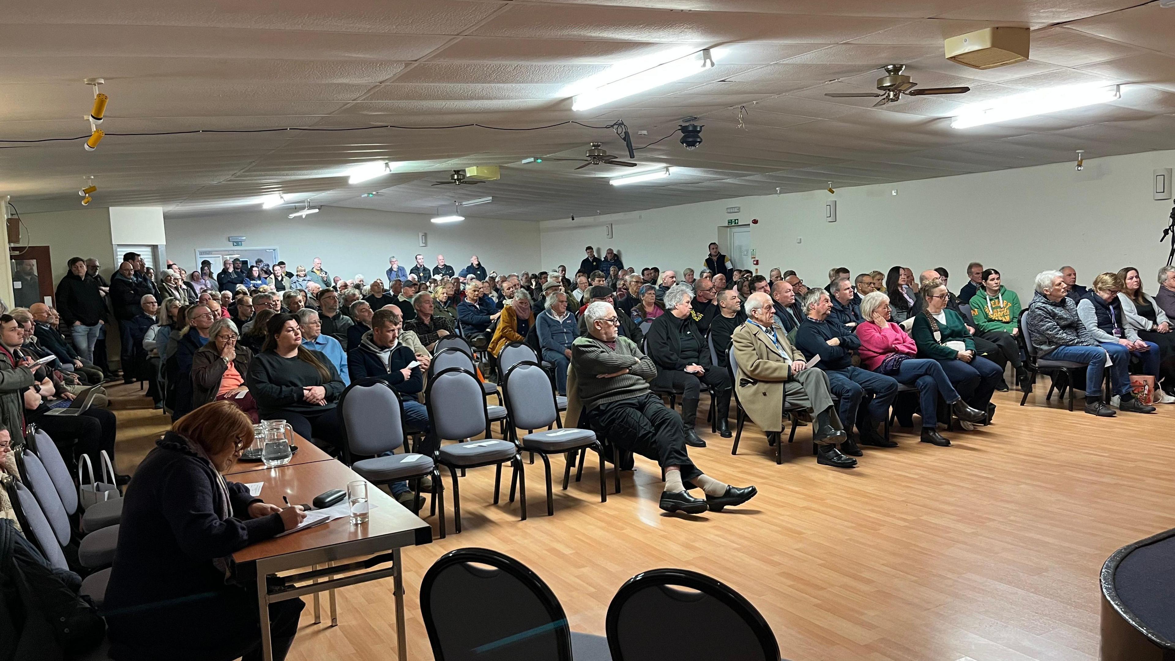 People seated in a village hall-type building. 