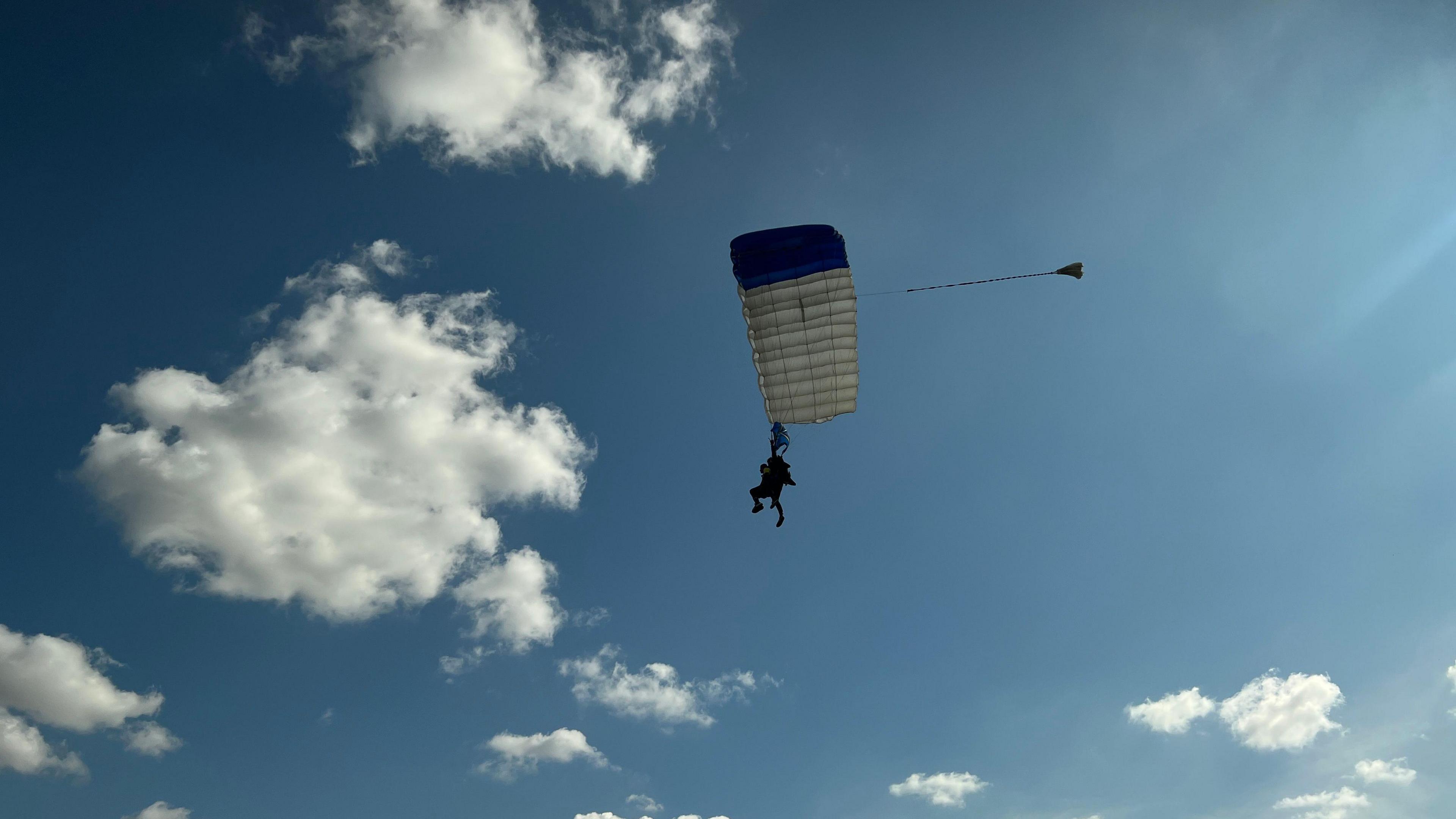 Dan Perkins parachuting with a white and red parachute, with blue sky and white clouds