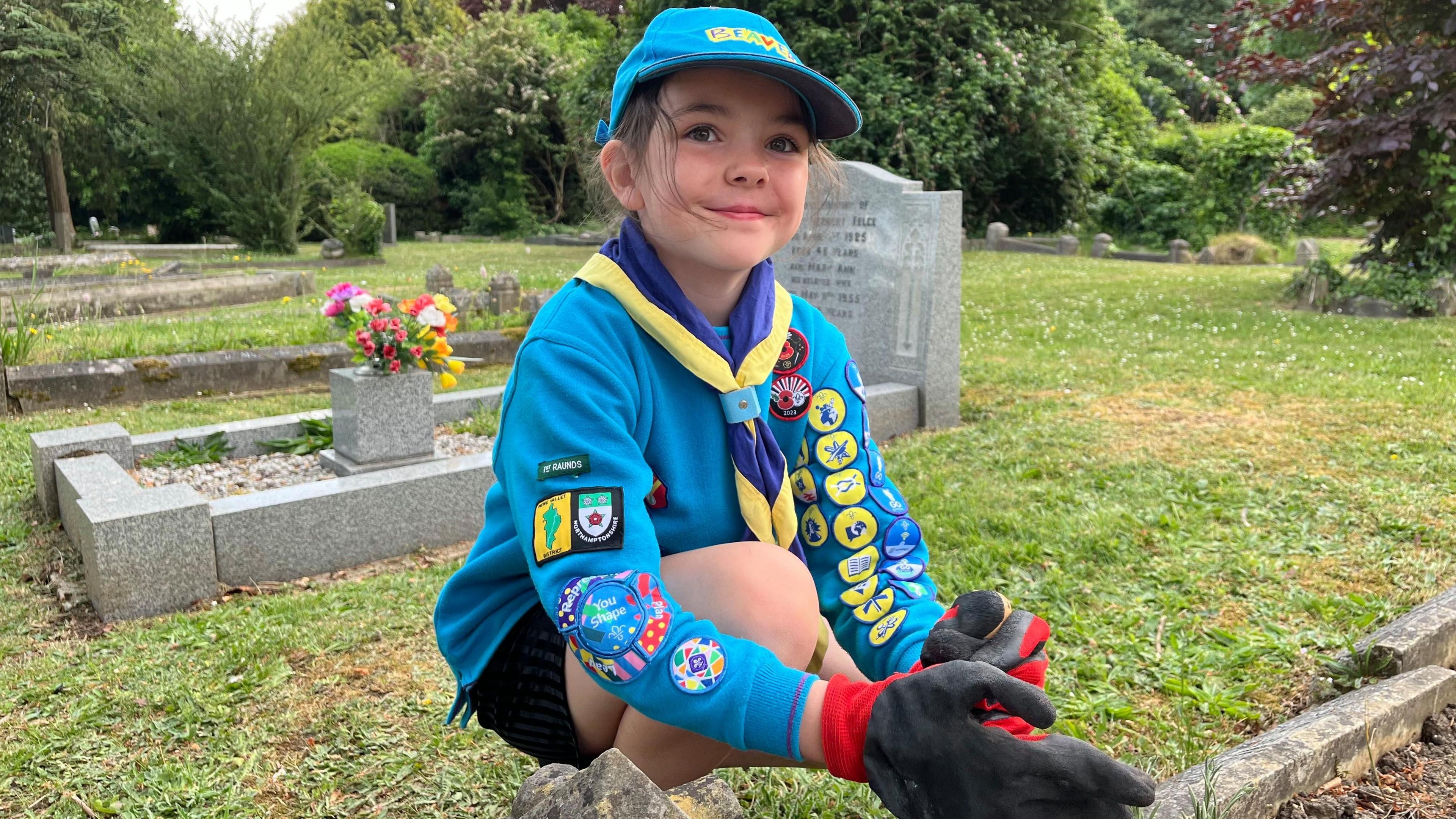 Girl in blue jumper crouched down next to a grave