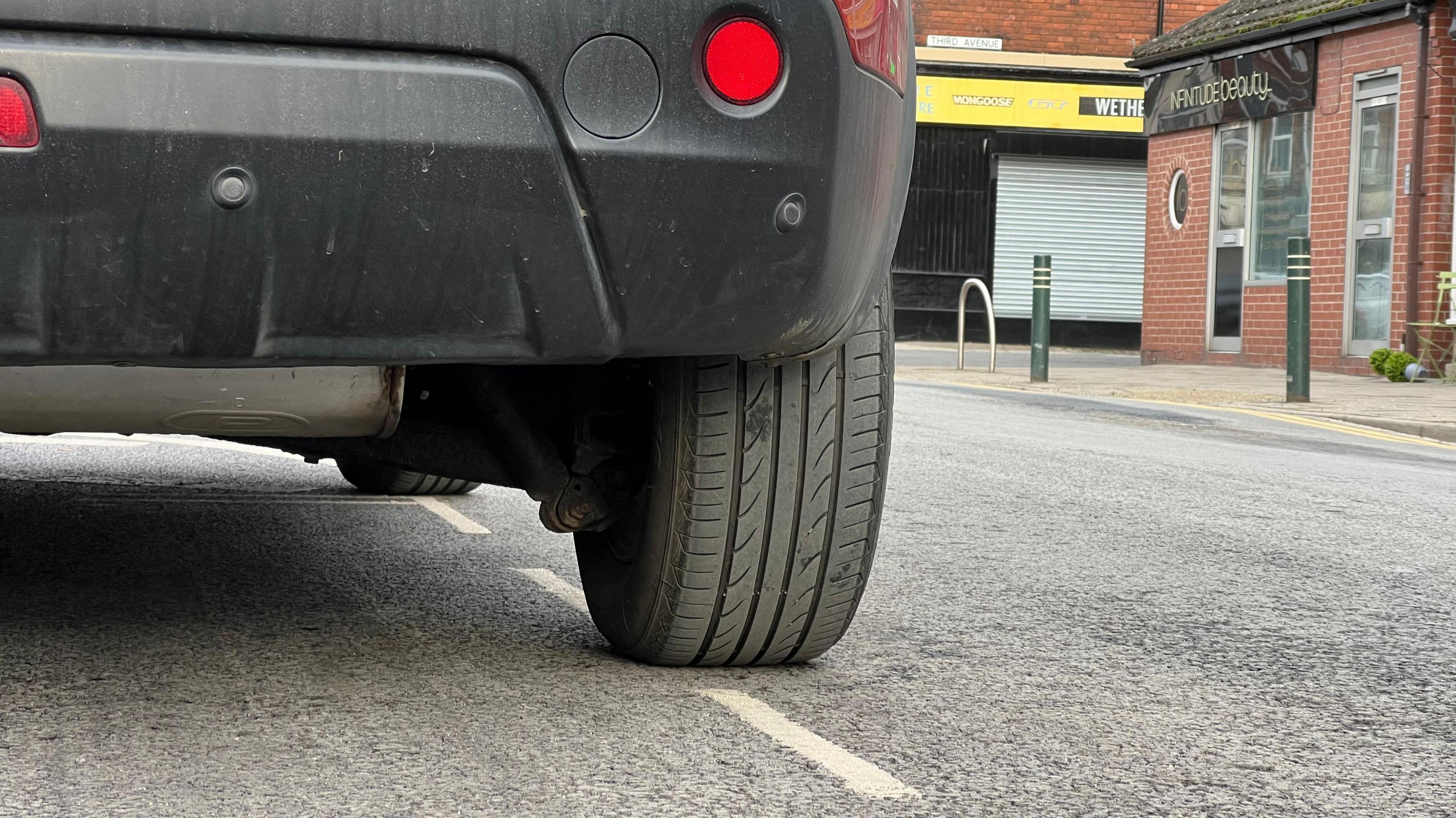 A parked black car can be seen with its tyre over the edge of the white parking bay lines on the road. 