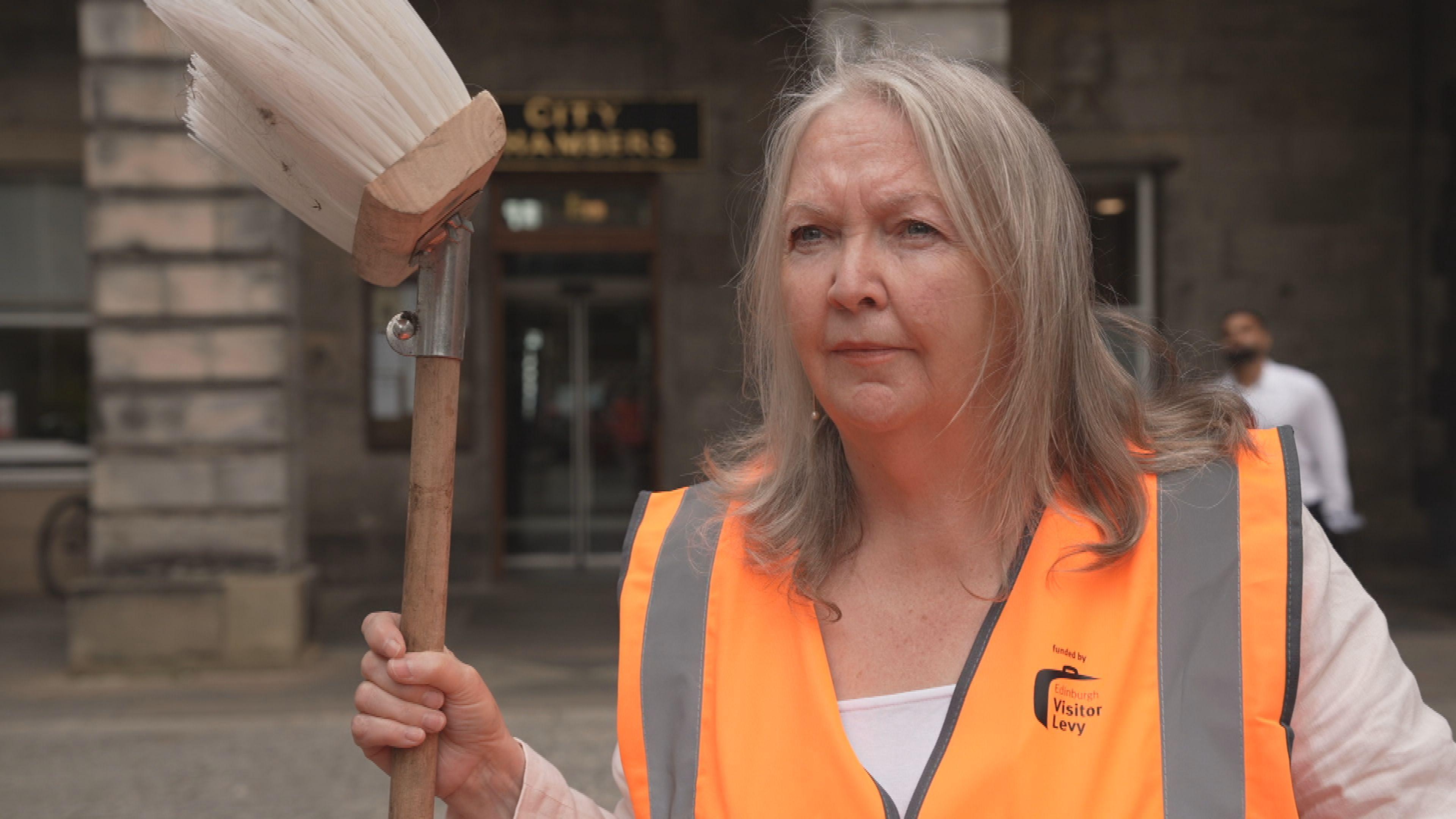 Council leader Jane Meagher holding a broom and wearing an orange hi-viz jacket.