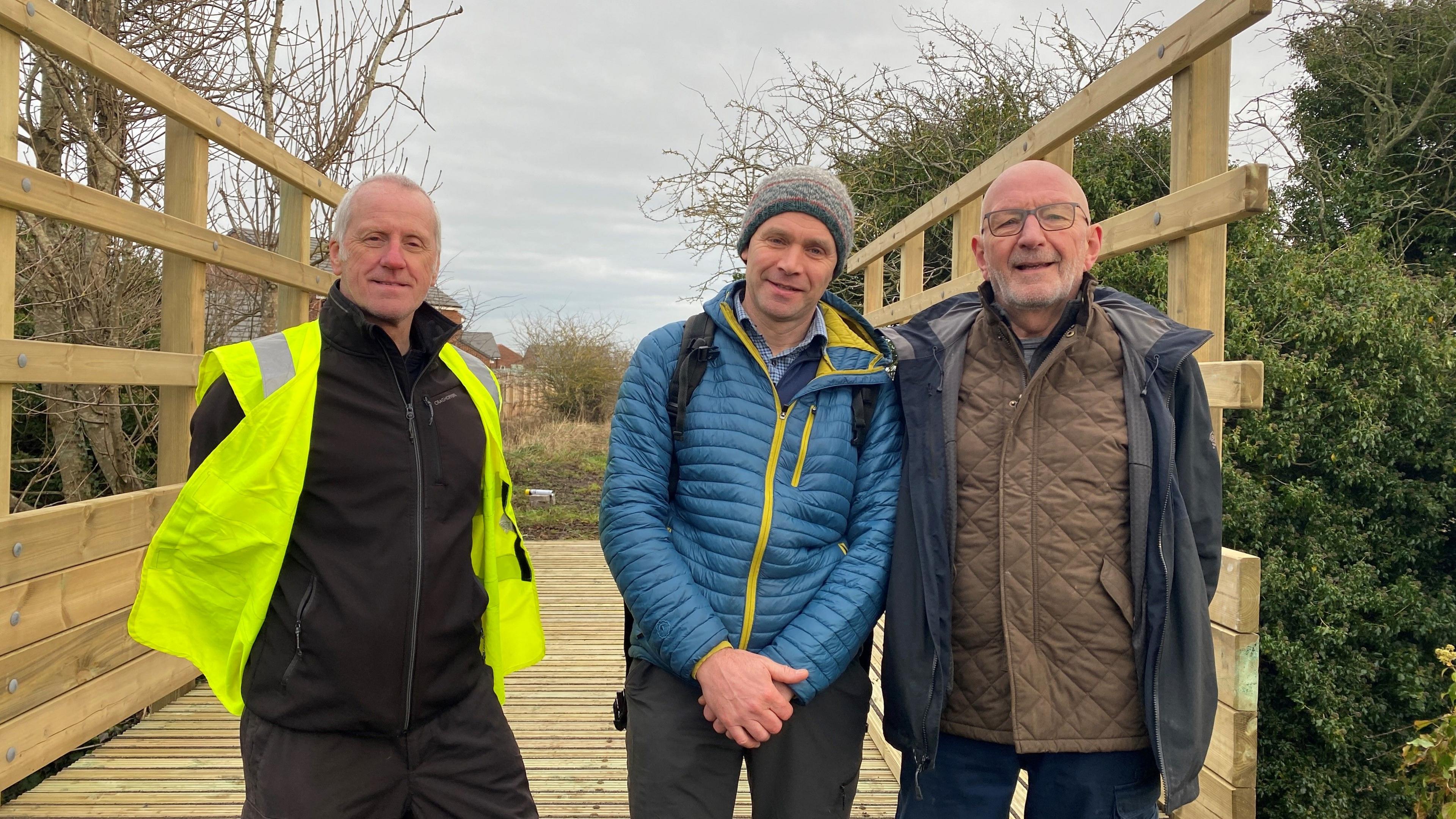 Stewart Oades, Martin Swinbank and another man stand in front of the new bridge which is wooden and about four metres long 