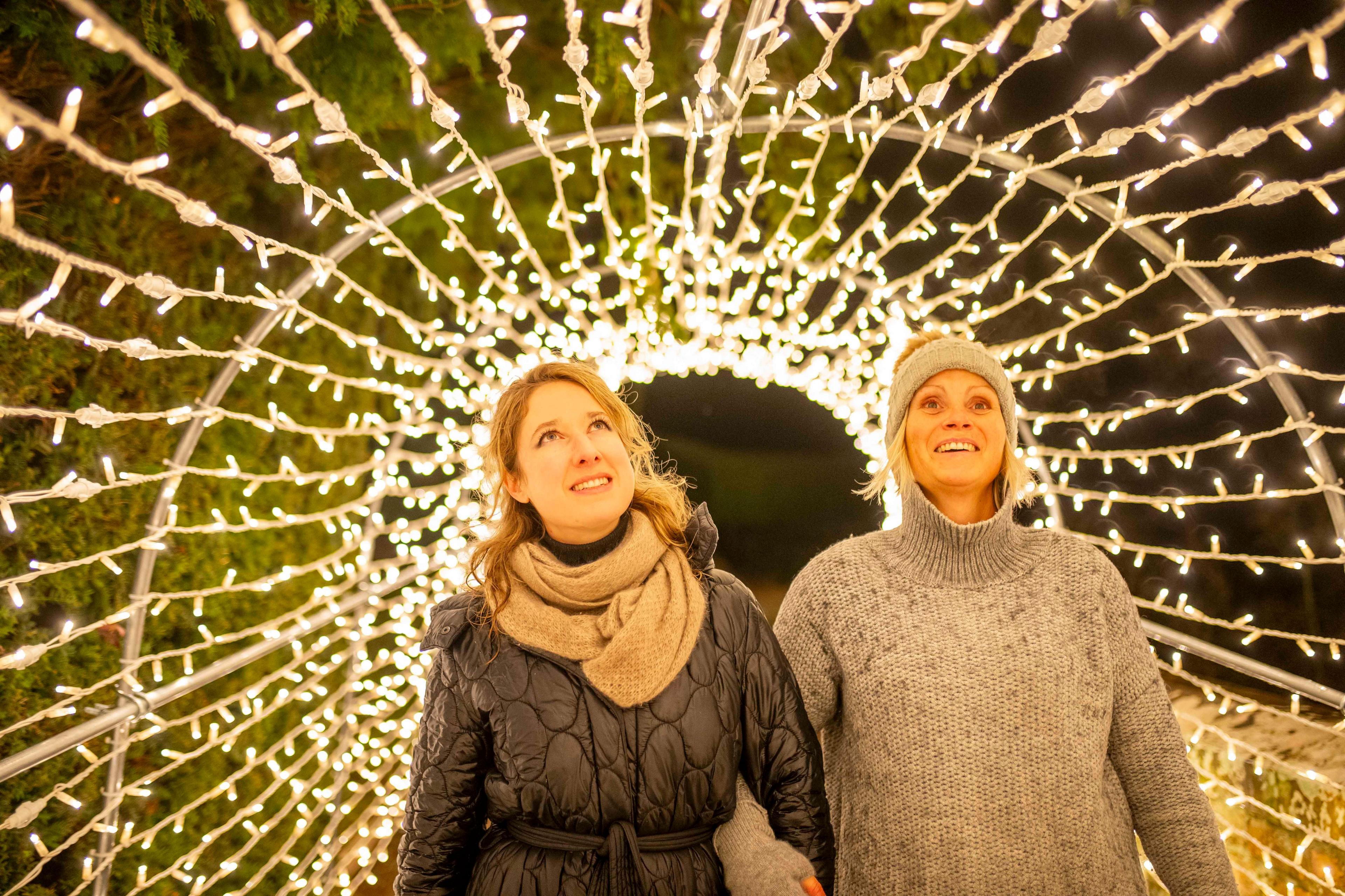 Two woman look up at a tunnel of lights as they walk through it