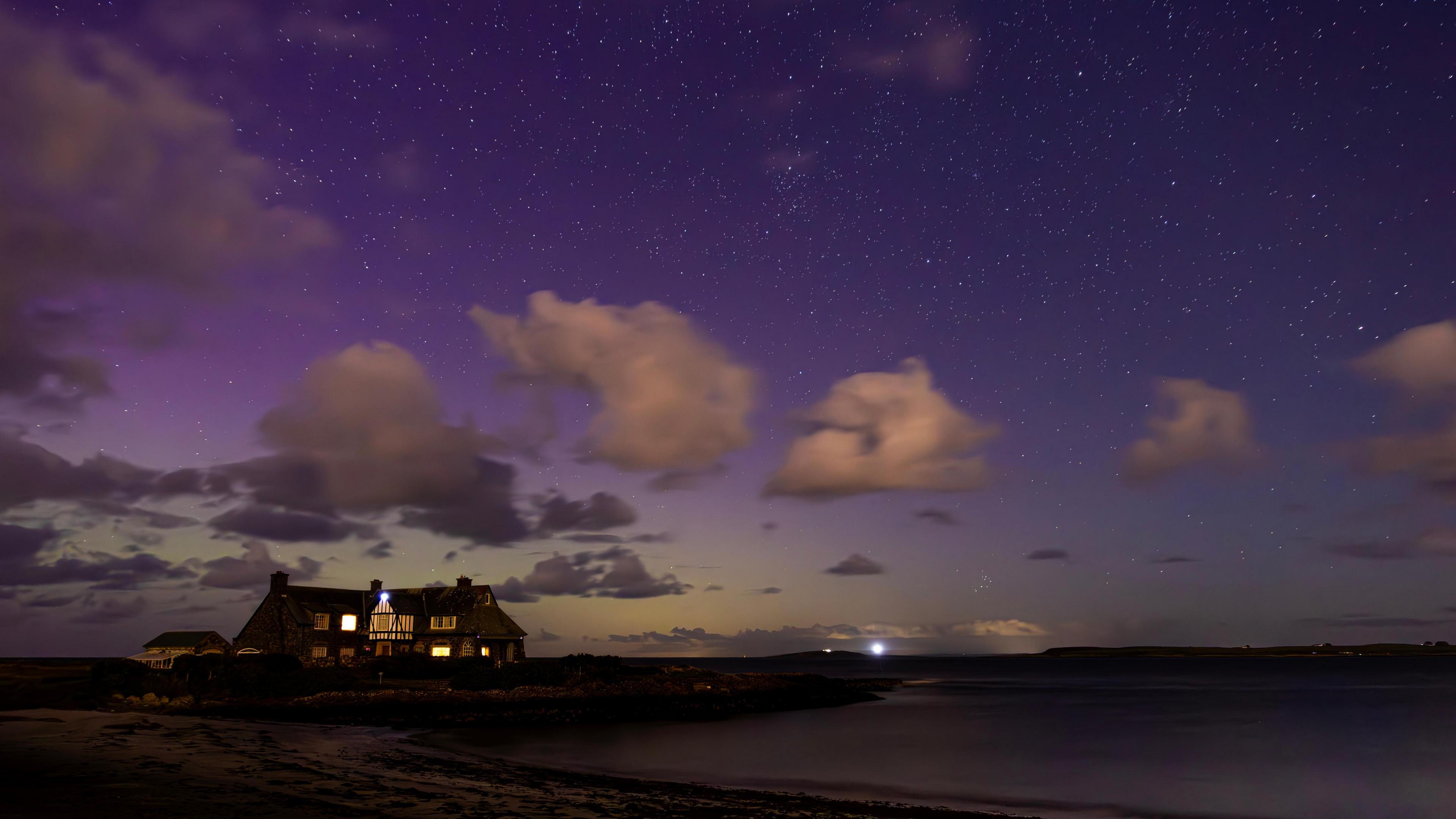 A house sits on the beach, the sky above is a purple glow, not the traditional appearance of the northern lights