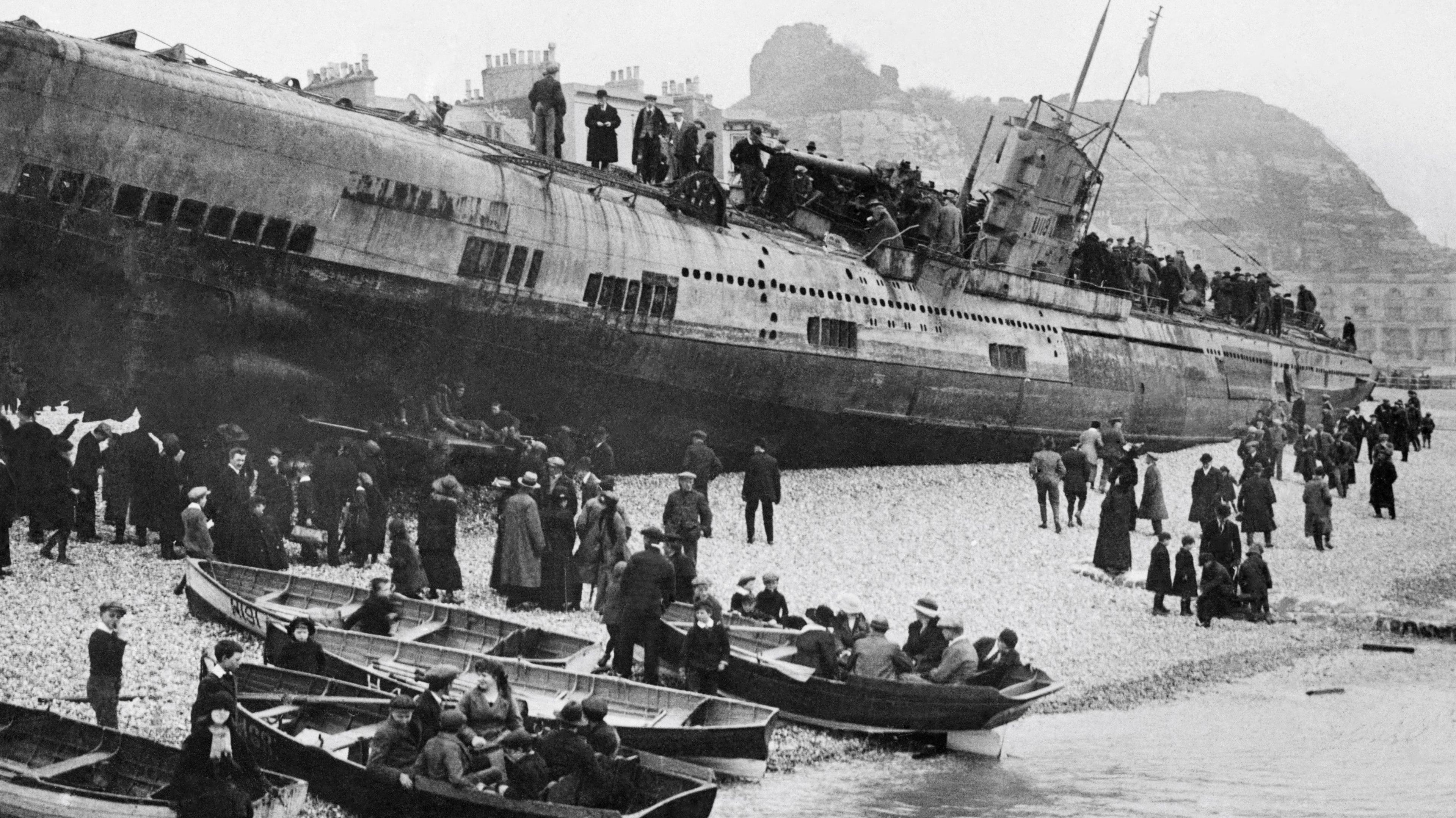 A black and white archive picture of a submarine in shallow waters on rocky of Hastings beach. People have climbed on top of the vessel and others are on the beach looking up at the craft. Some are in boats on the shore.