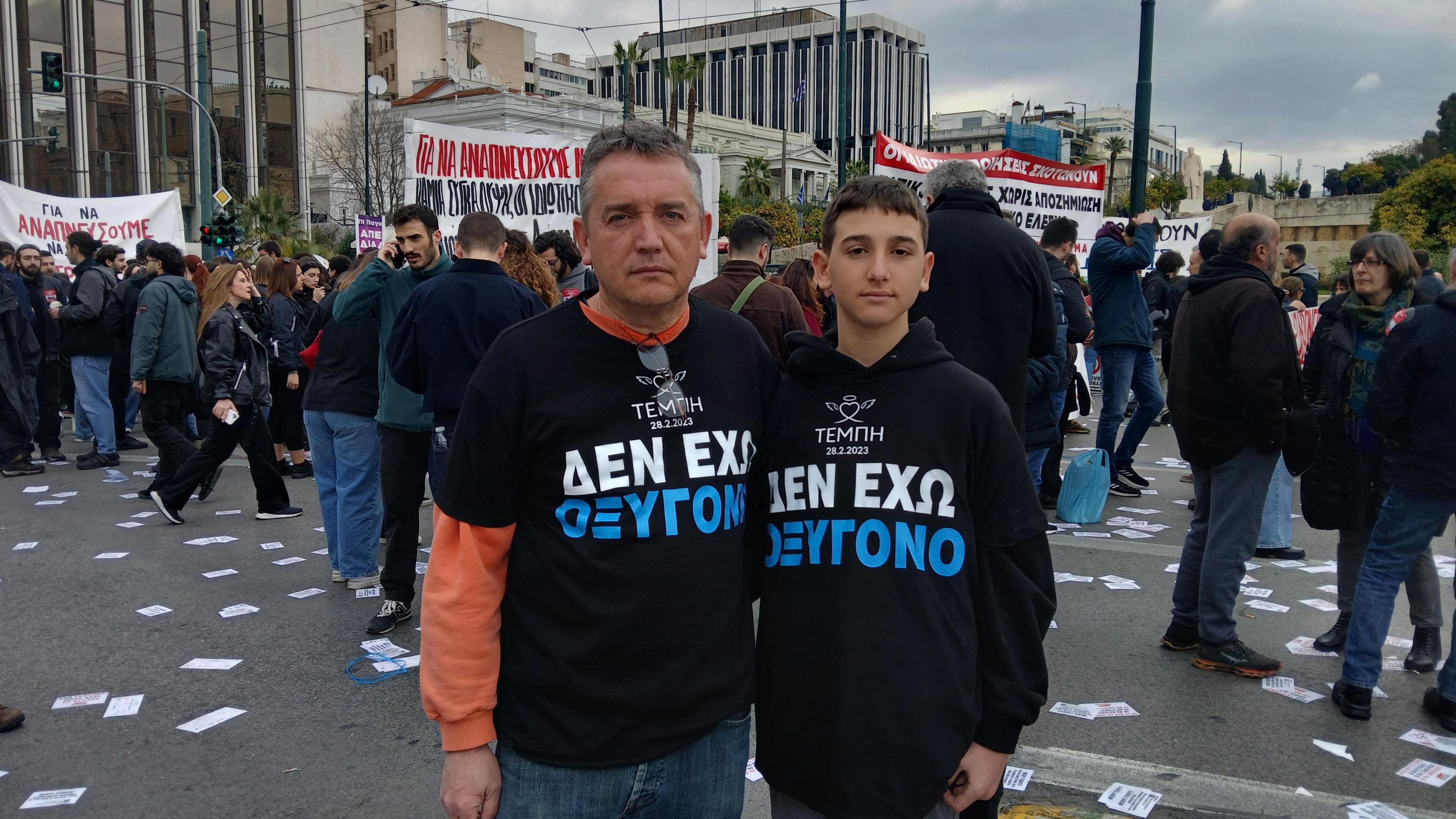 A man and his son wear black t-shirts that read in Greek - "I have no oxygen"