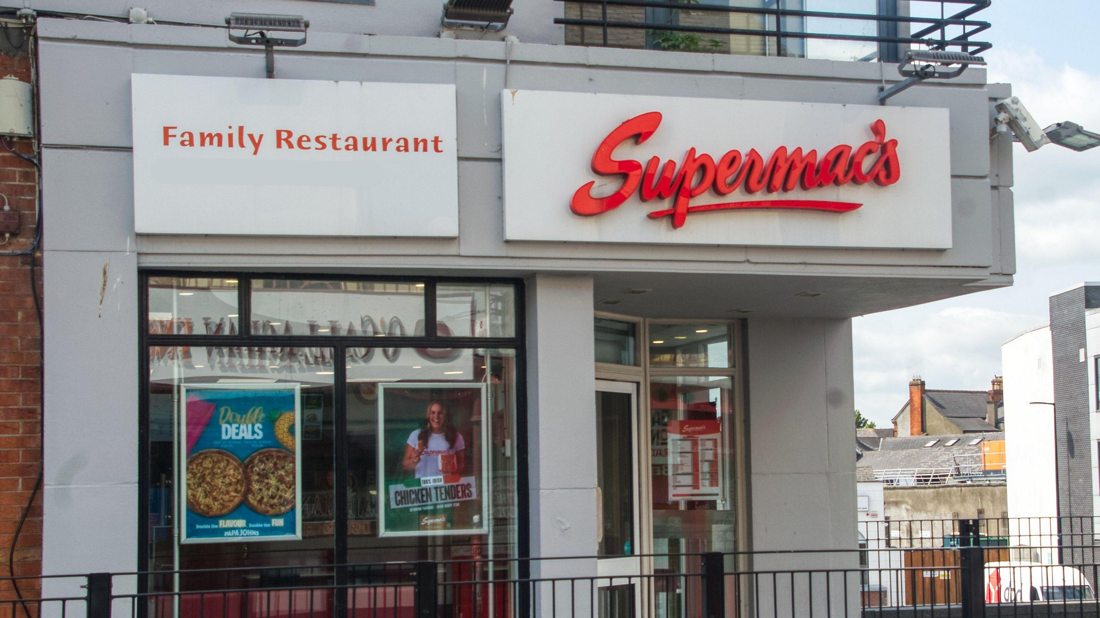The exterior of a Supermac's fast food restaurant in Ireland. A large red letter sign shows the name of the business above a door and glass fronted store