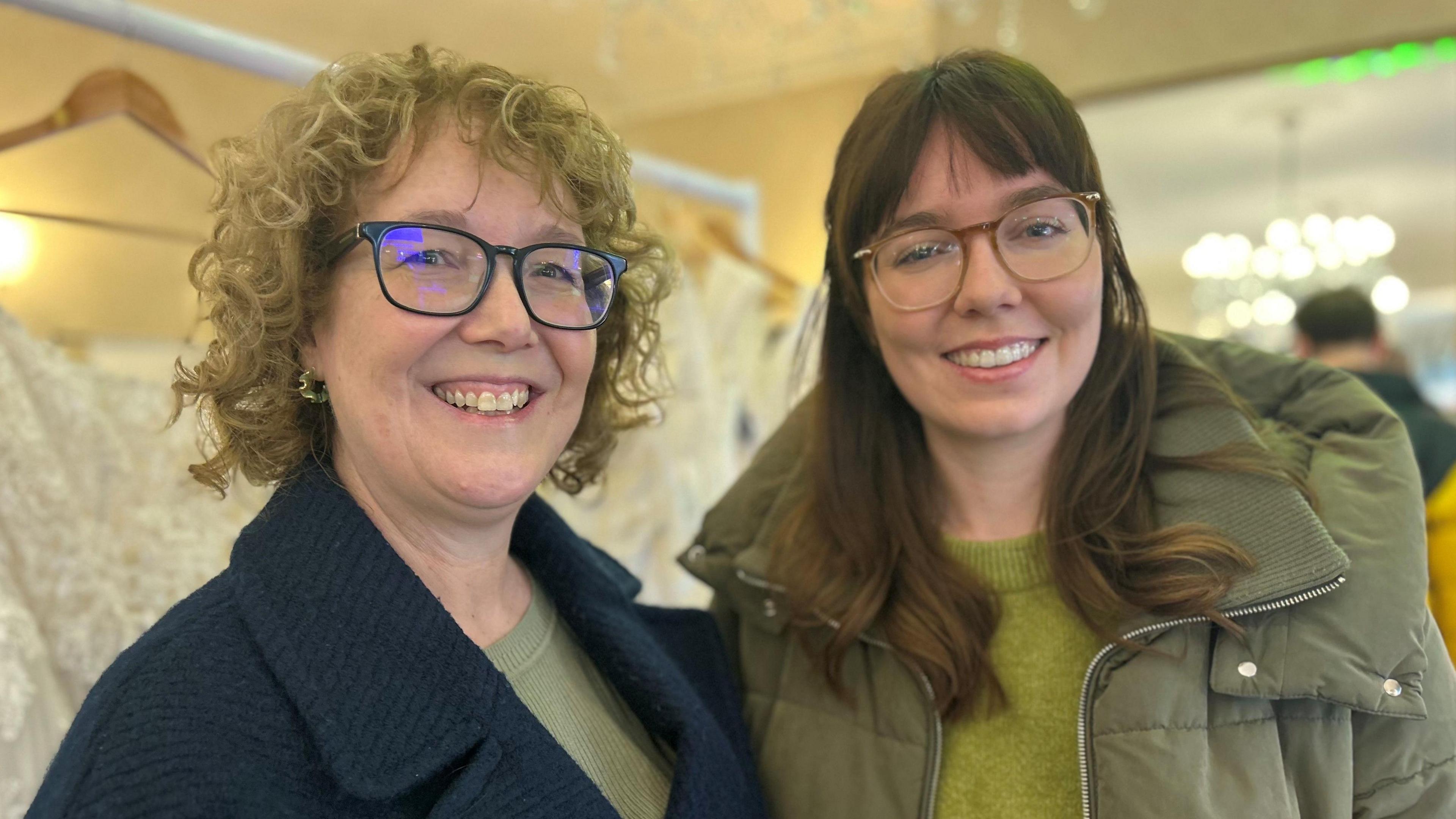 Mae Nia Donnelly ar y chwith a Bethan Donnelly ar y dde ac mae'r ddwy yn gwenu. Mae'r ddwy hefyd yn gwisgo sbectol. Mae gan Nia wallt cyrliog golau a chot las. Mae Bethan yn gwisgo cot werdd ac mae ganddi wallt hir brown.
