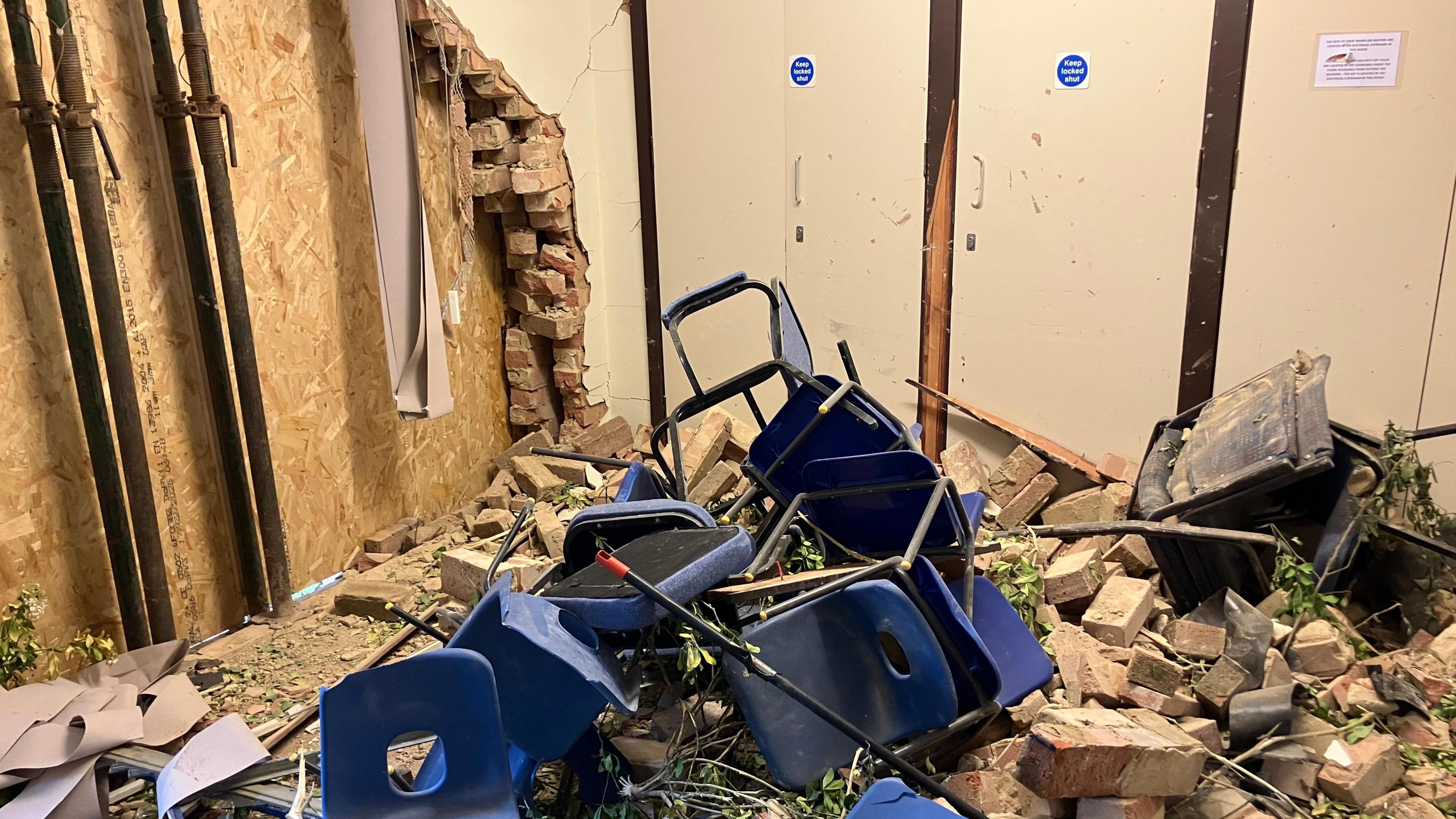 Wrecked meeting room- with bricks and debris on the floor- blue chairs and table damaged and thrown in the rubble