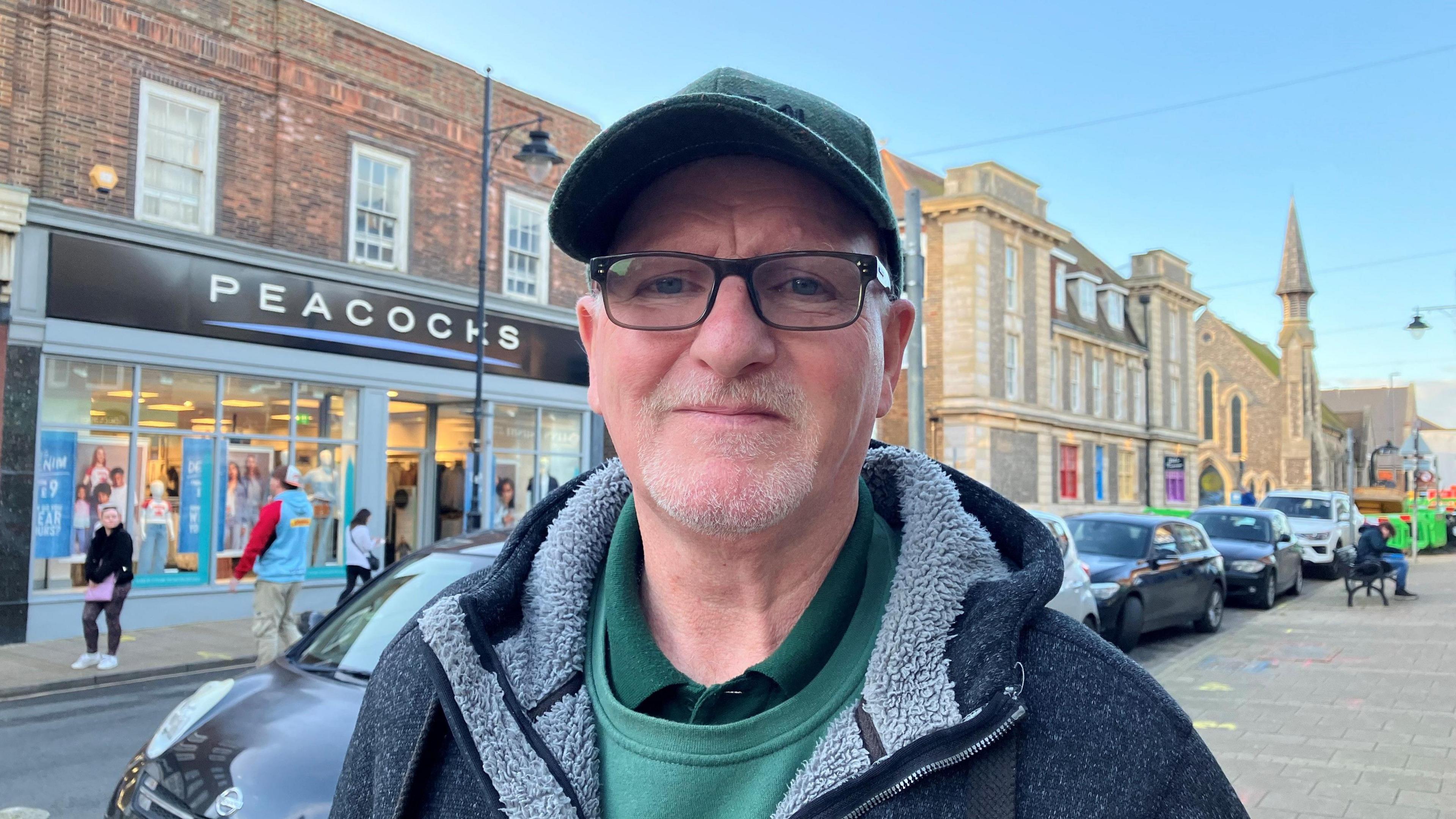 Gerry Brown looks at the camera. He is wearing a cap and glasses and has a hoodie on with a furry lining.