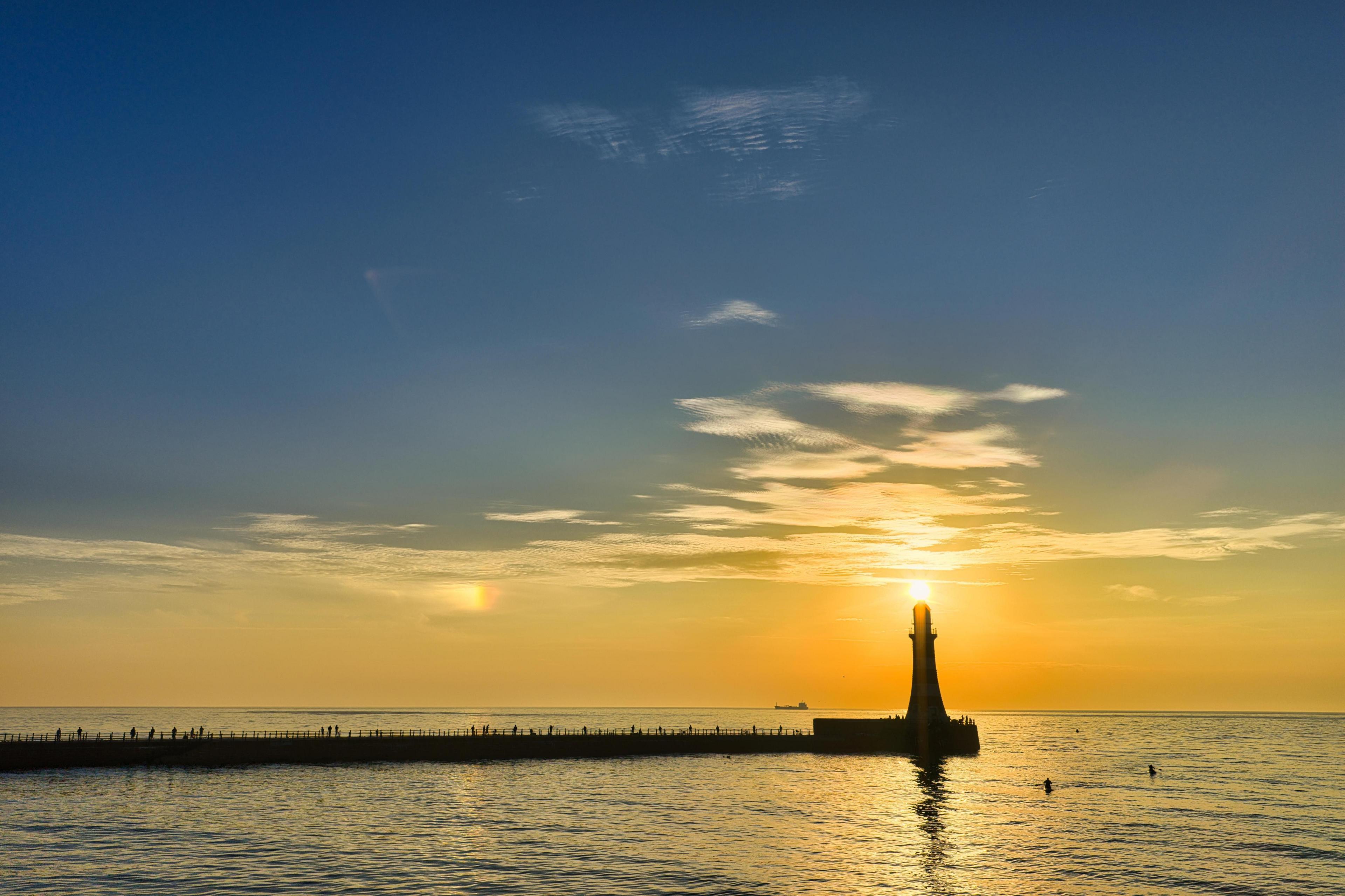 The sun rises above a lighthouse in Sunderland. The sun is reflected in the sea.