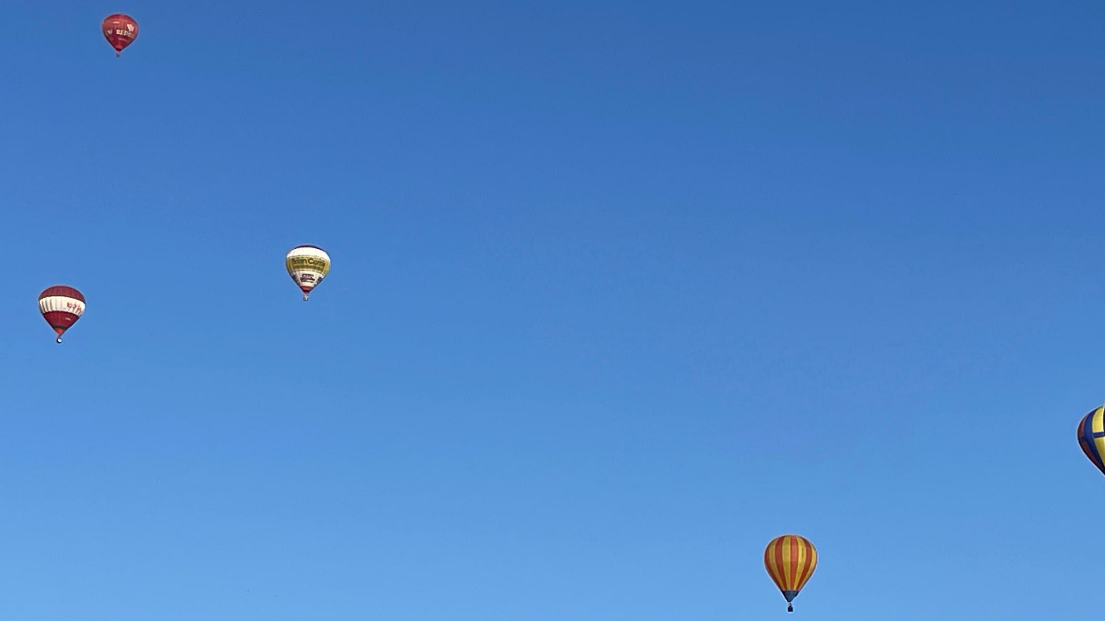 Four colourful balloons float in the sky on a clear blue day. 