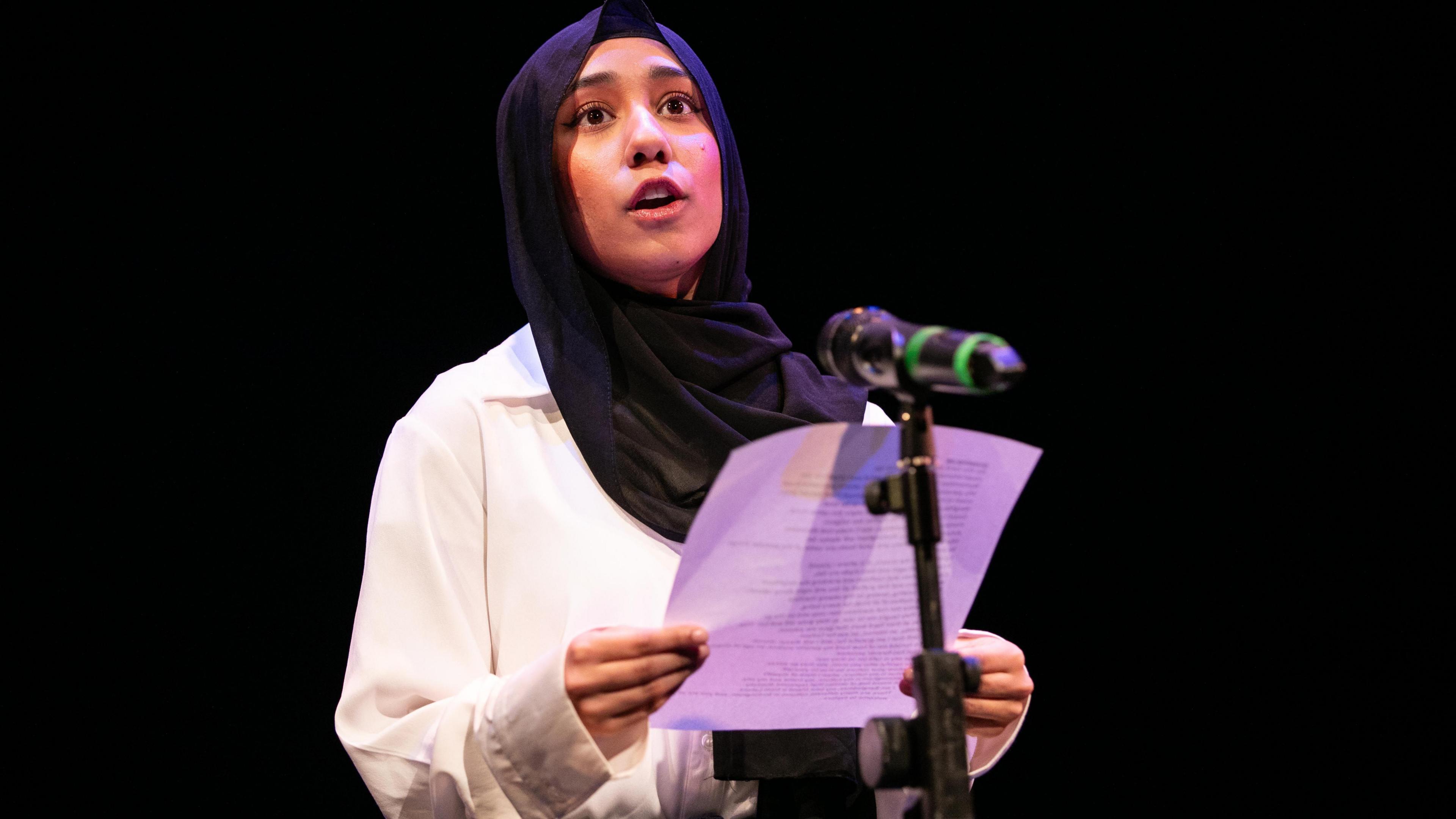 A woman speaking a poem on stage in front of a microphone 