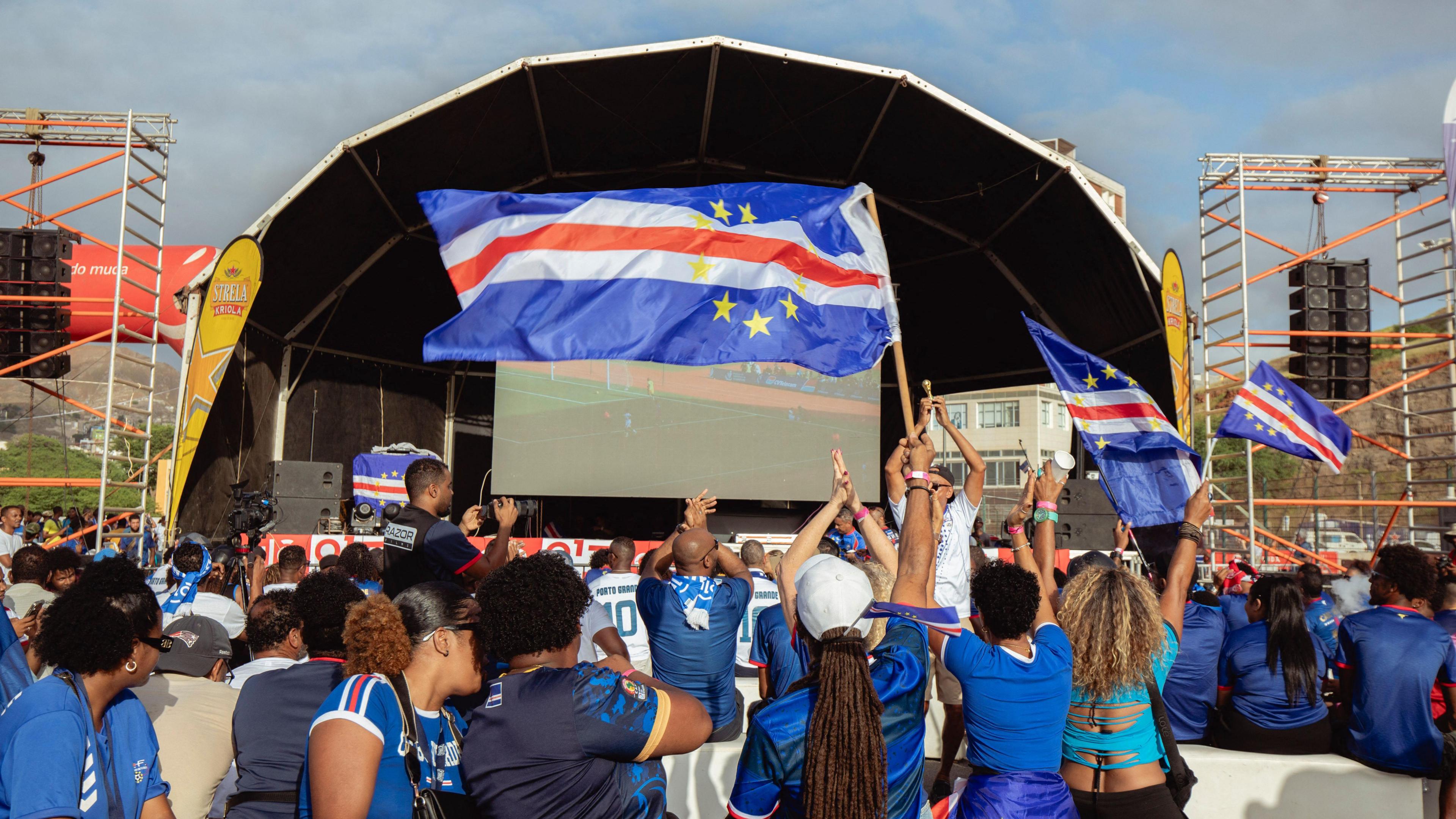 Fans stand in front of a video screen holding Cape Verde flags