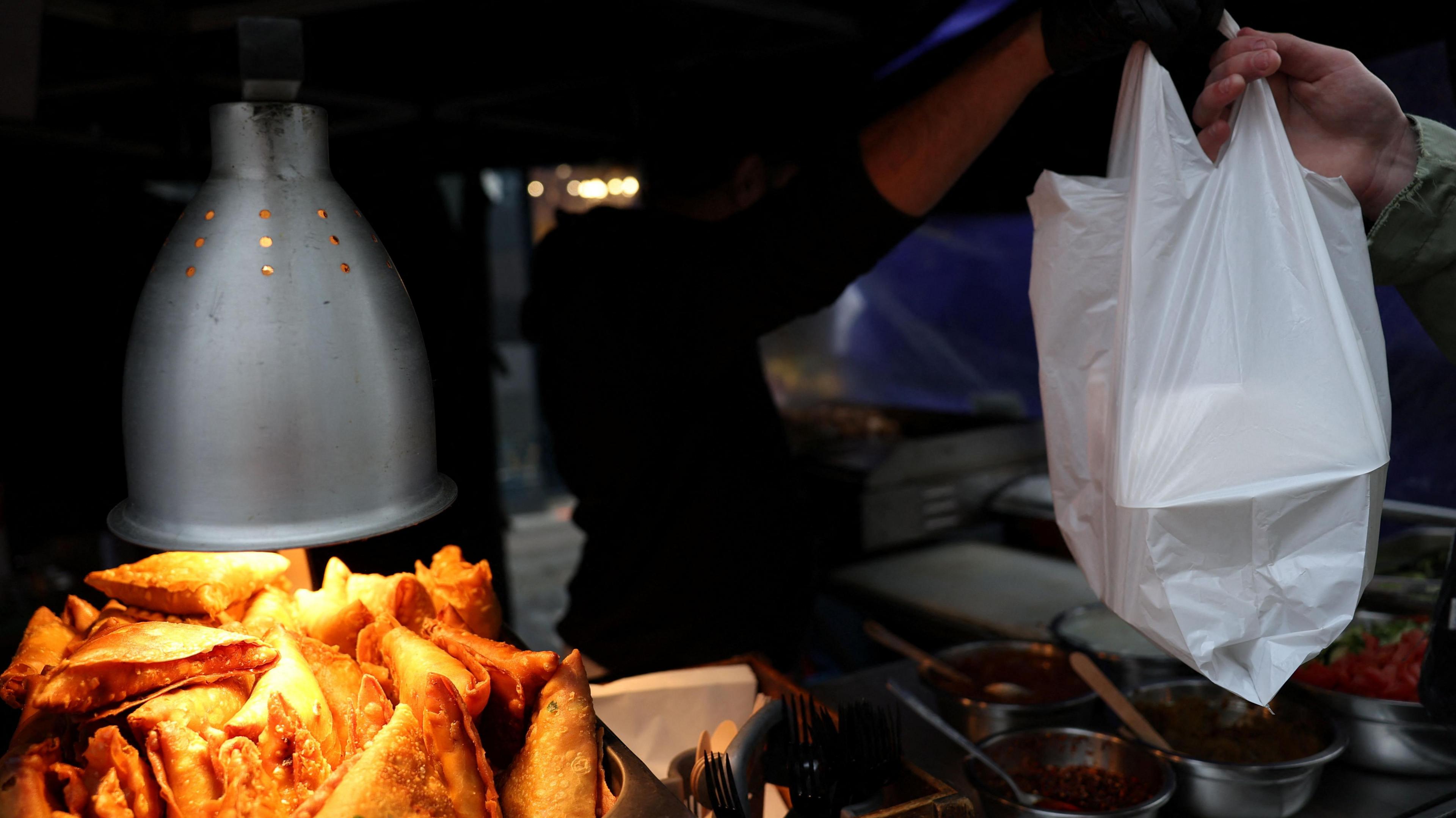 Takeaway counter with somozas on display and a customer receiving a white carrier bag full of takeawy food.