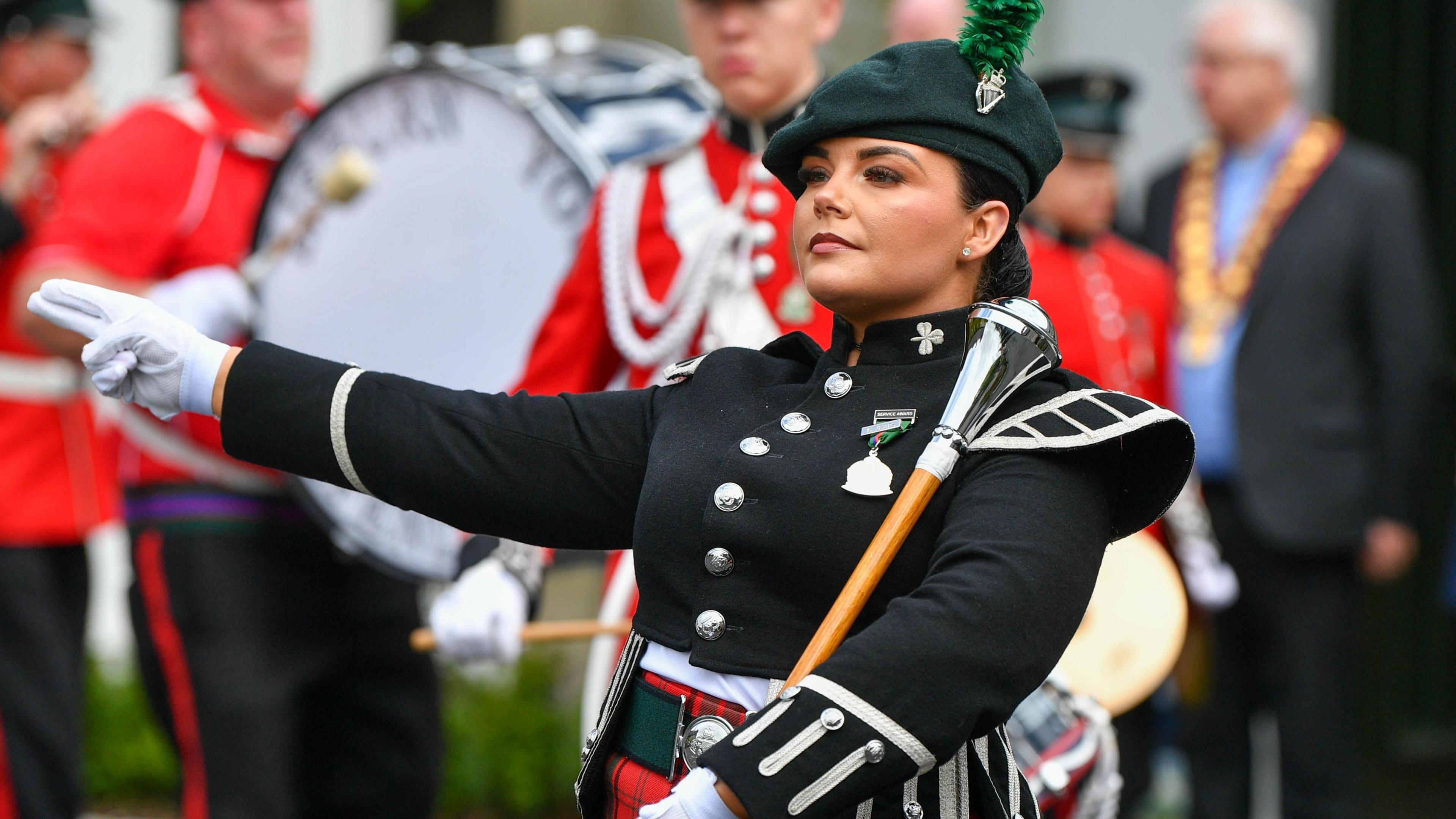 A band member wearing a black jacket and red tartan skirt holds a 