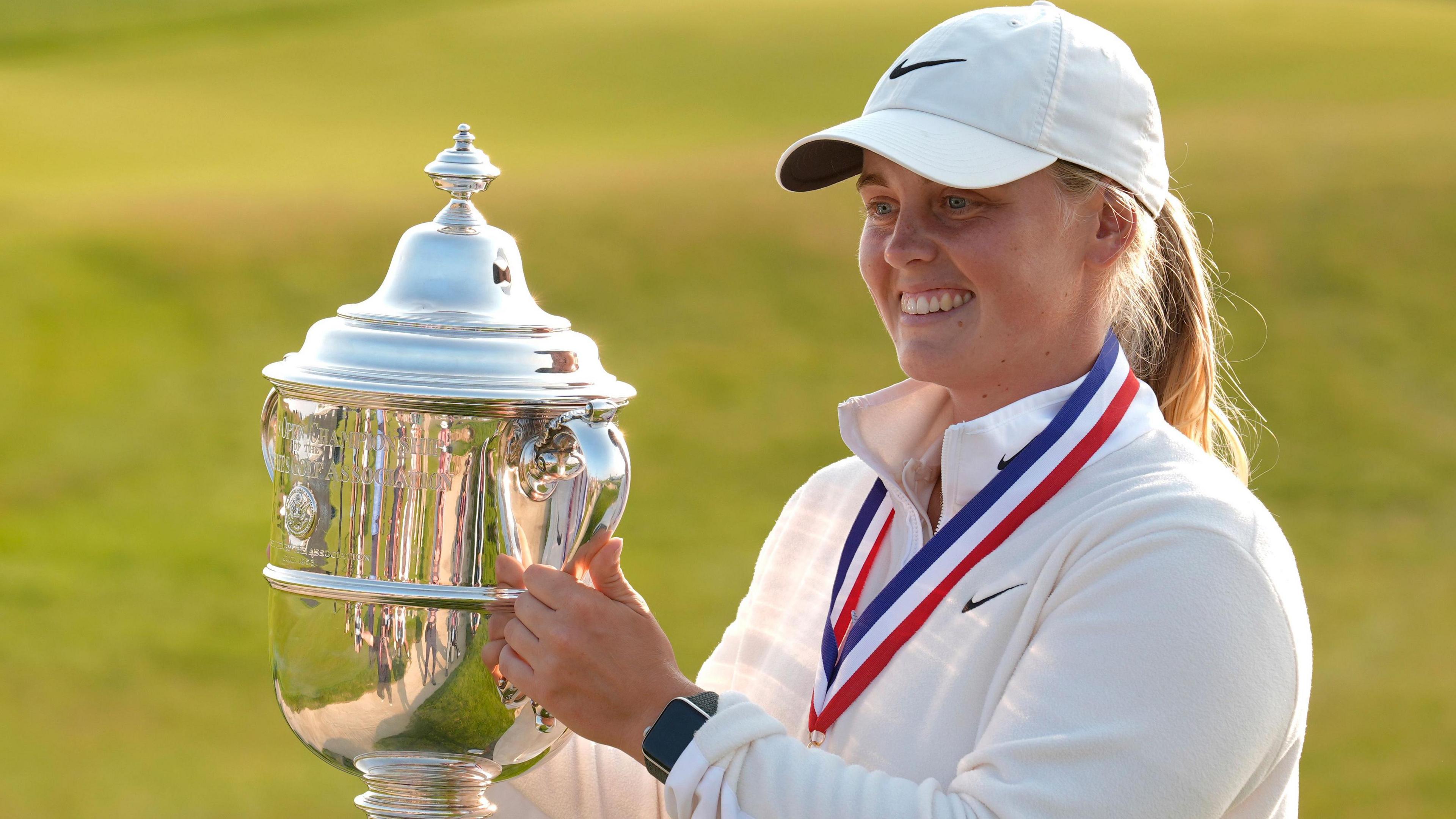 Maja Stark, wearing a baseball cap, holds the US Women's Open trophy