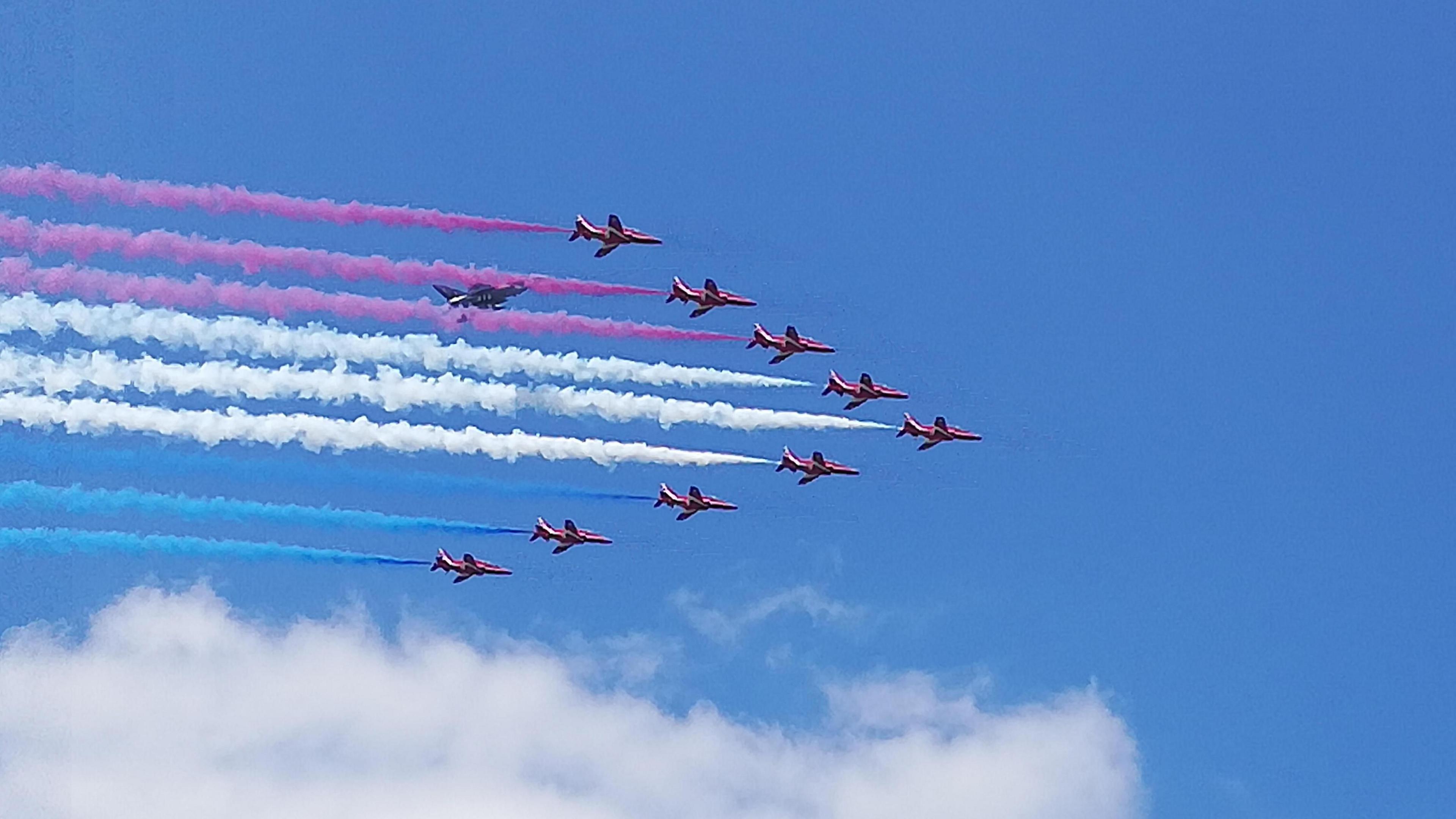 Blue skies with the distinctive arrow formation of the RAF Red Arrows and red, white and blue smoke trails