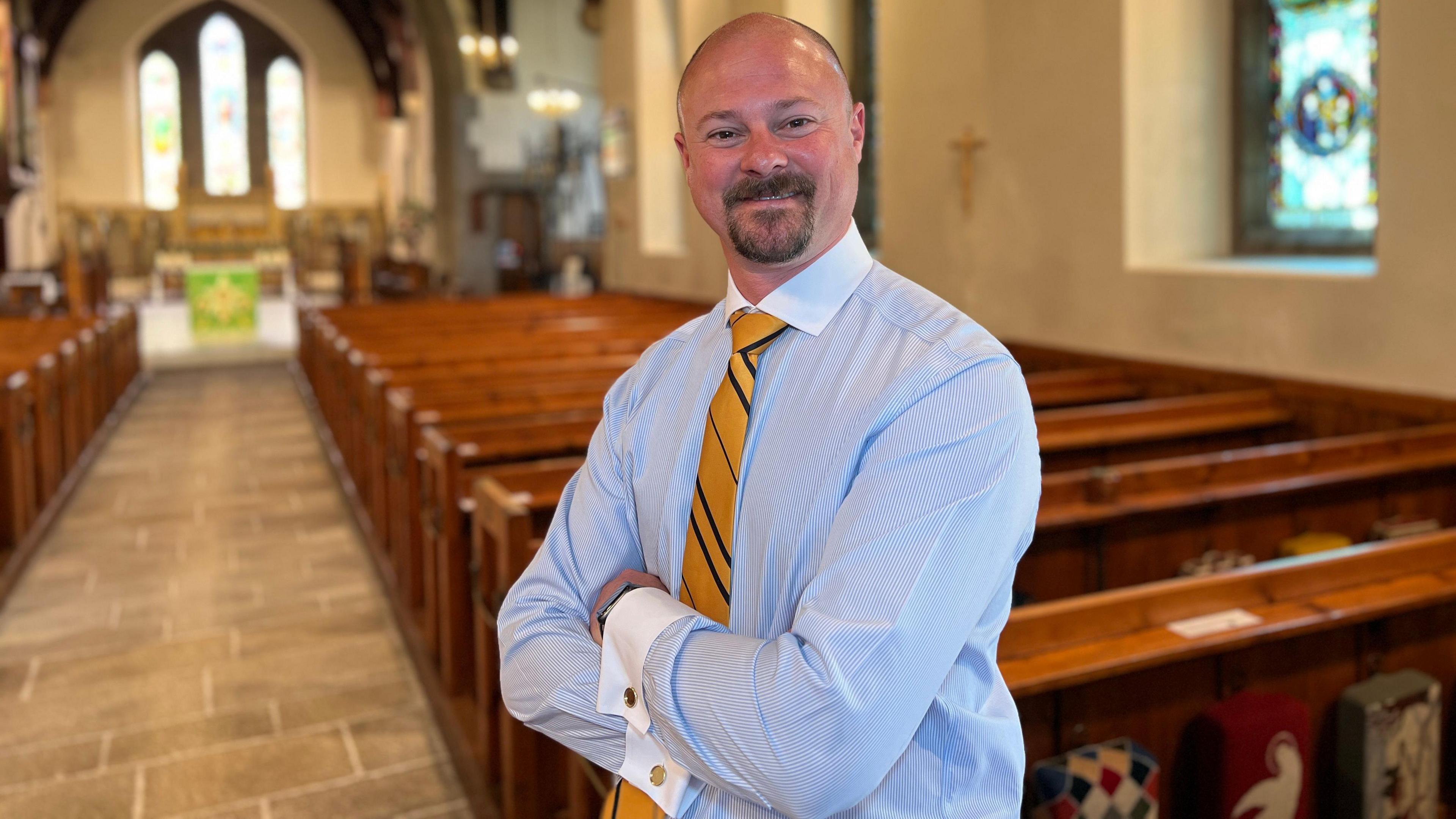 Alex smiles at the camera with the pews behind him and the altar in the background