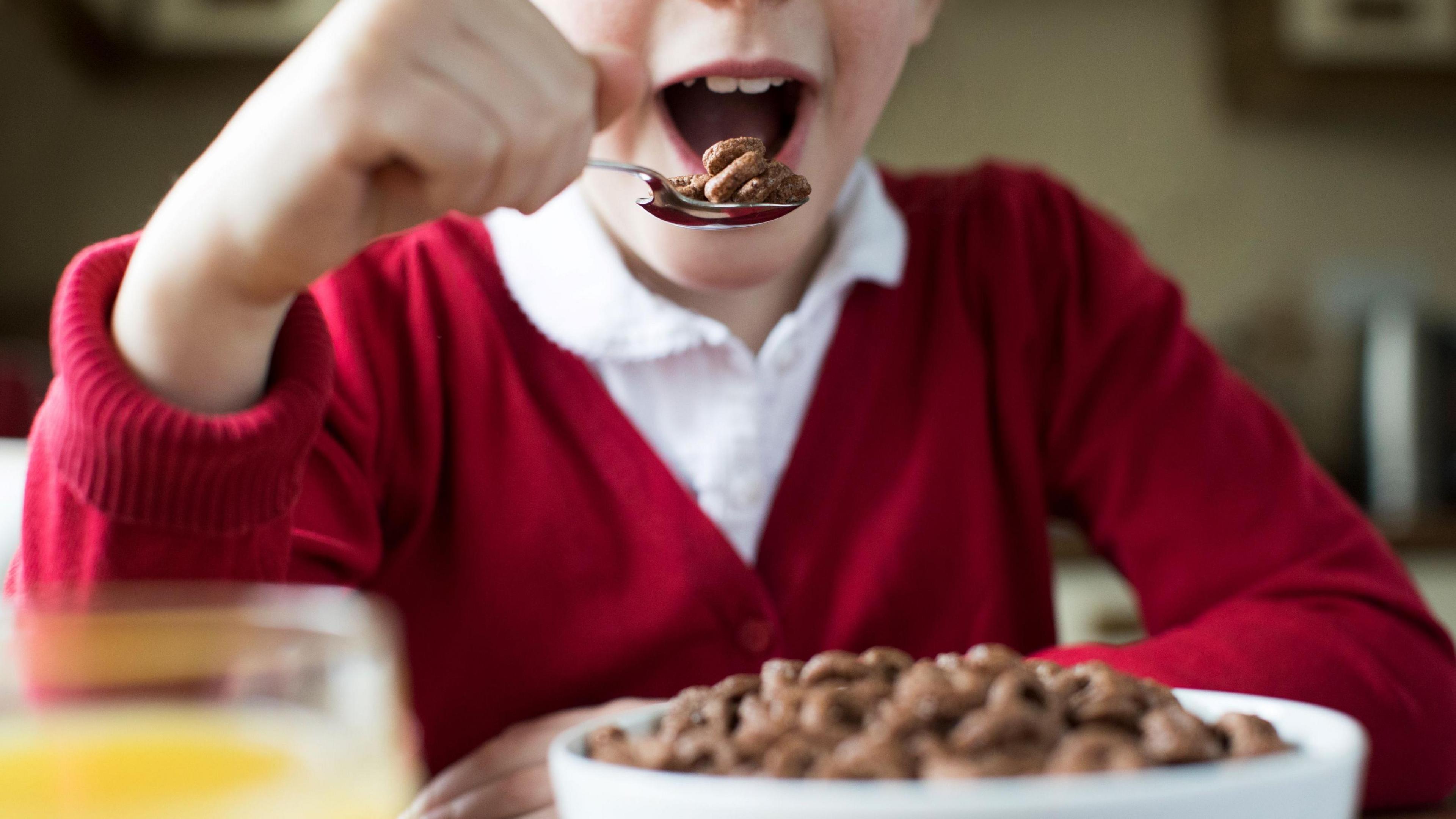 A stock picture of a child in school uniform eating a bowl of cereal