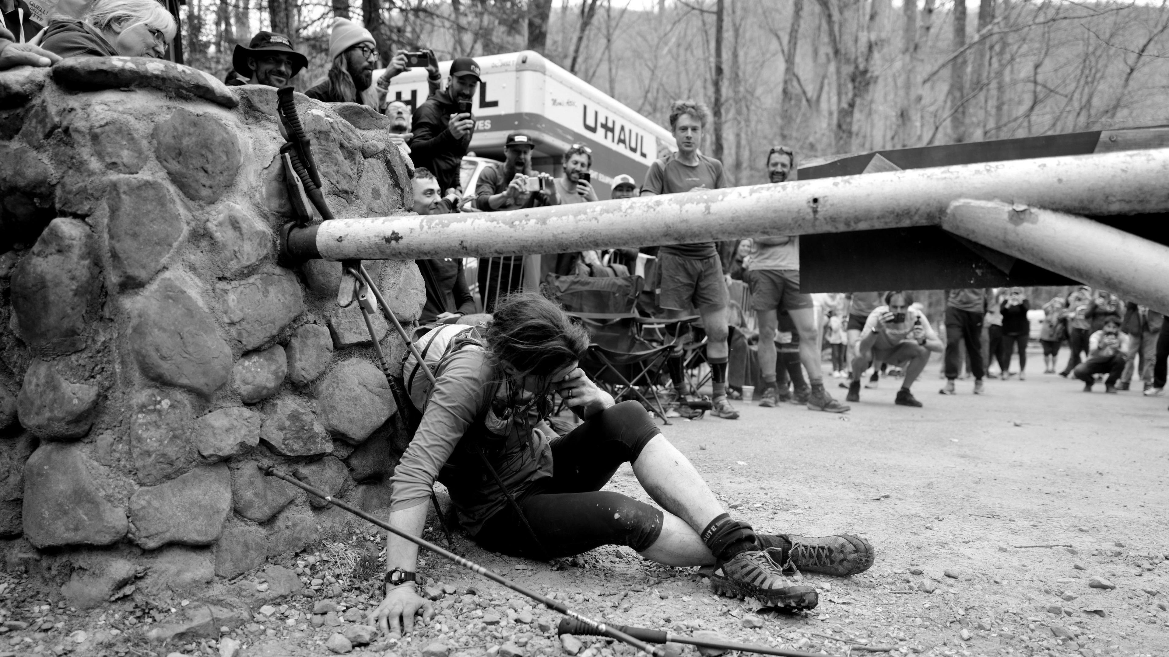 Jasmin Paris is slumped on the ground at the finish line. Her head is bowed and she is clearly very tired. She is wearing outdoor runing gear.