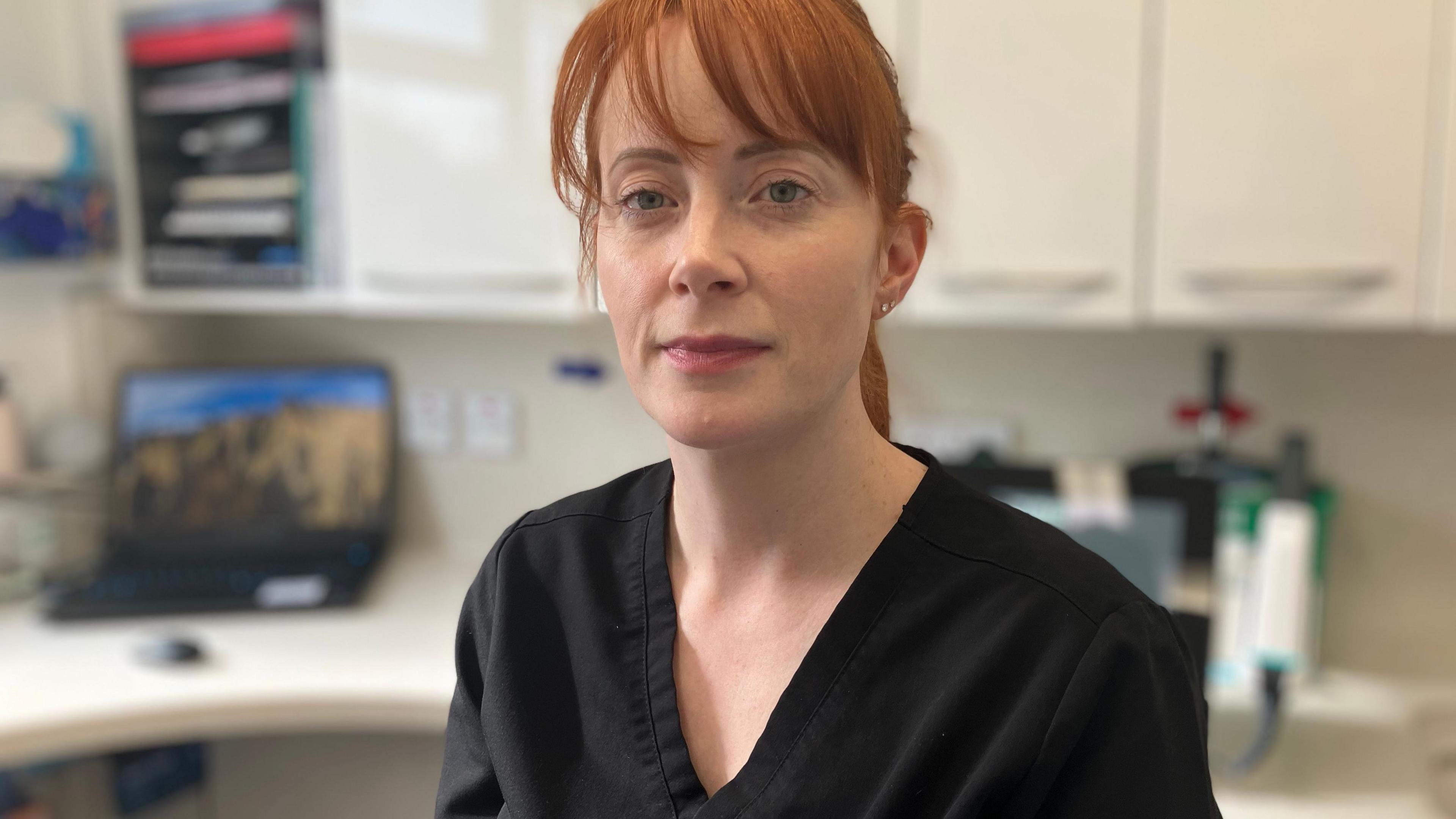 A red-haired woman in a black dental scrubs. 