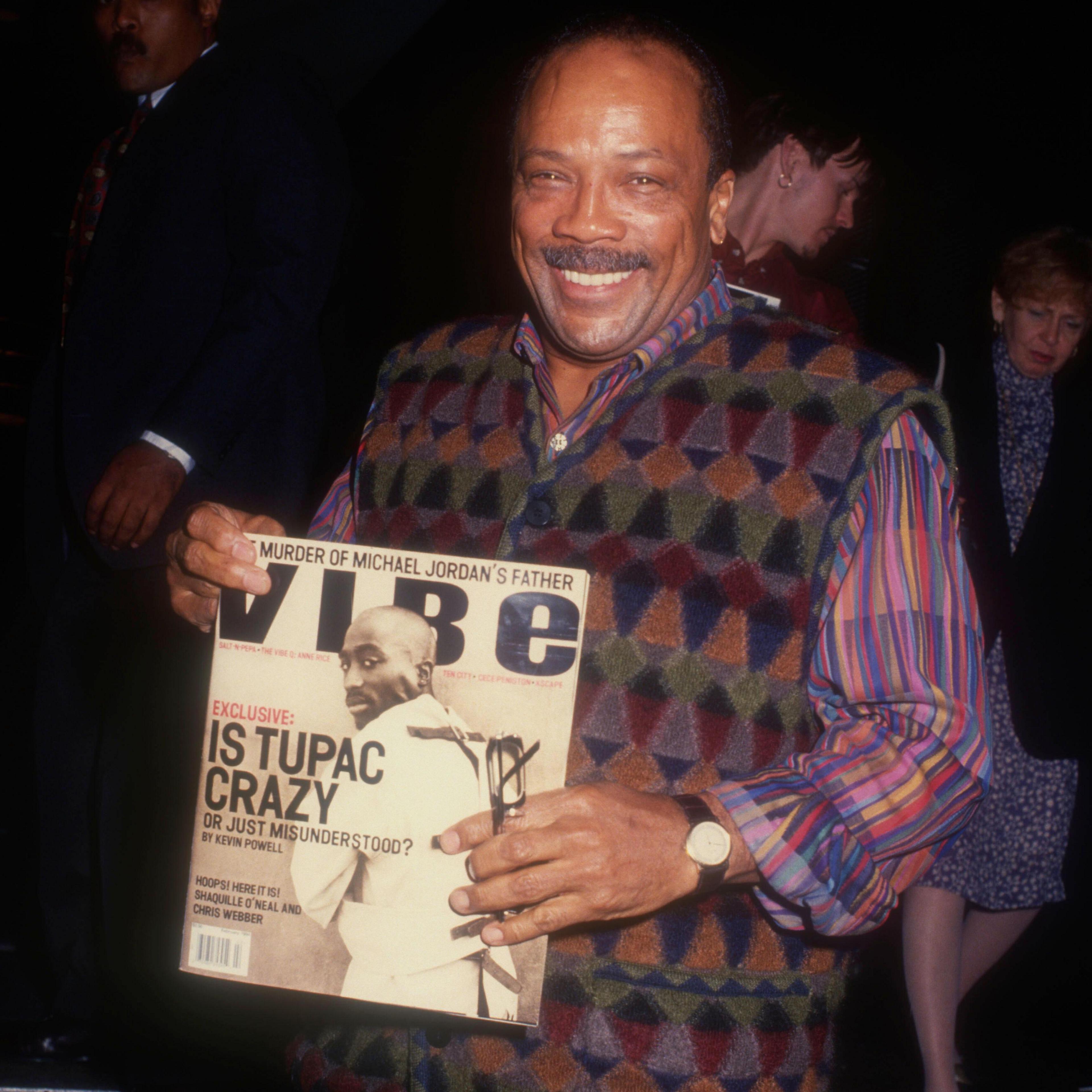 Quincy Jones holding up a copy of Vibe magazine with Tupac Shakur on the cover and the headline "Is Tupac crazy or just misunderstood?"