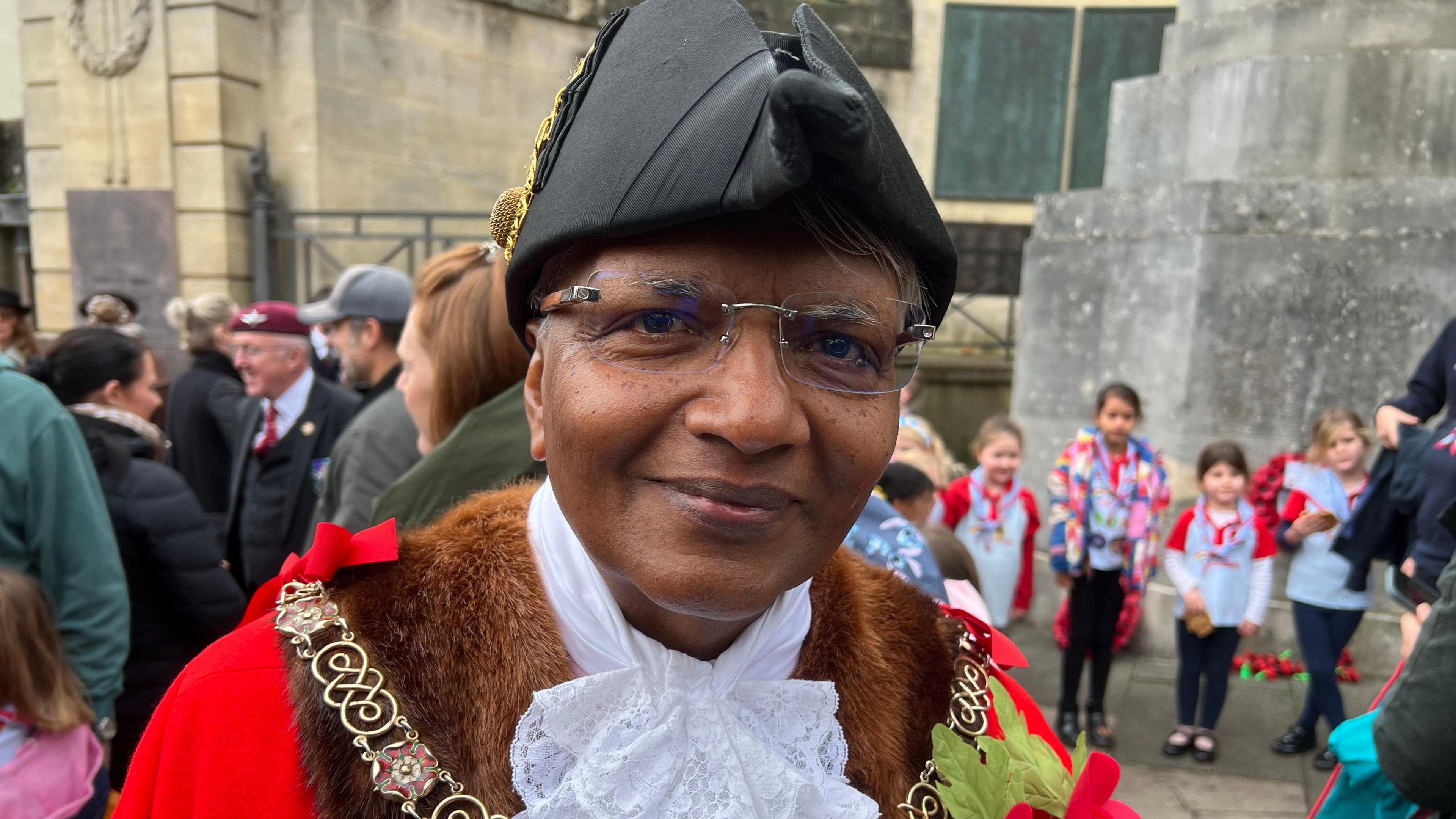 Bharat Pankhania. He is dressed in mayoral attire which includes a red robe and a black hat. He is looking at the camera and smiling.