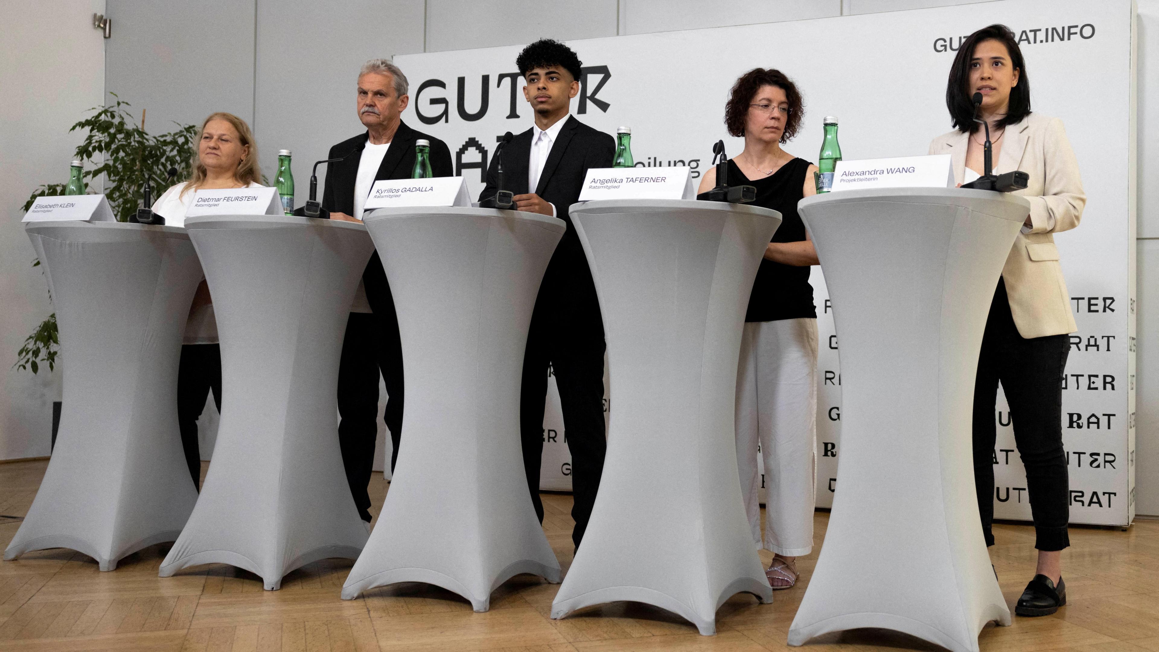 Five people standing behind lecterns