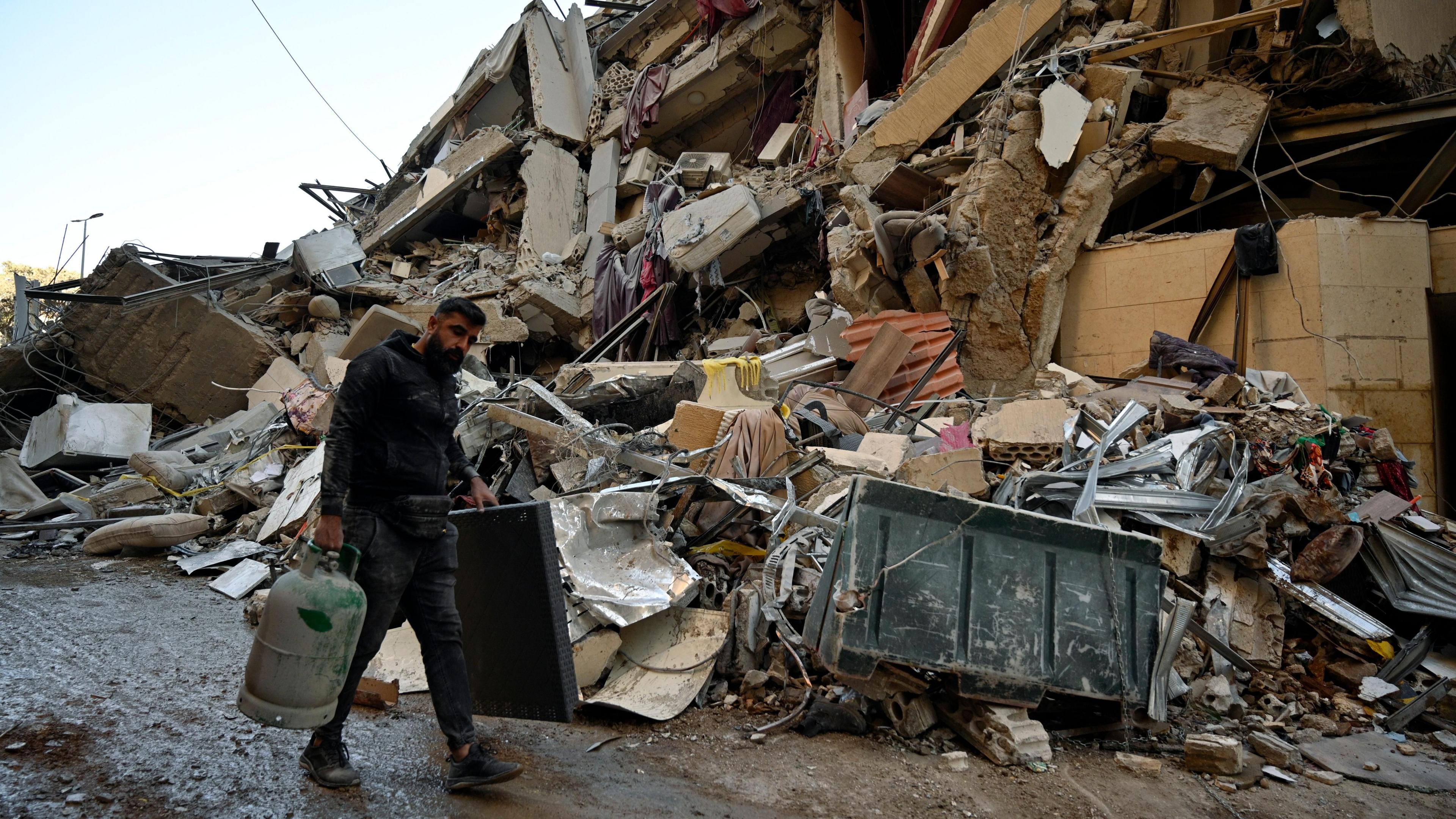 A man walks past a destroyed building in the Beirut suburb of Chiyah, Lebanon, following an Israeli strike that targeted a branch of the Hezbollah-linked Al-Qard Al-Hassan financial association (21 October 2024)