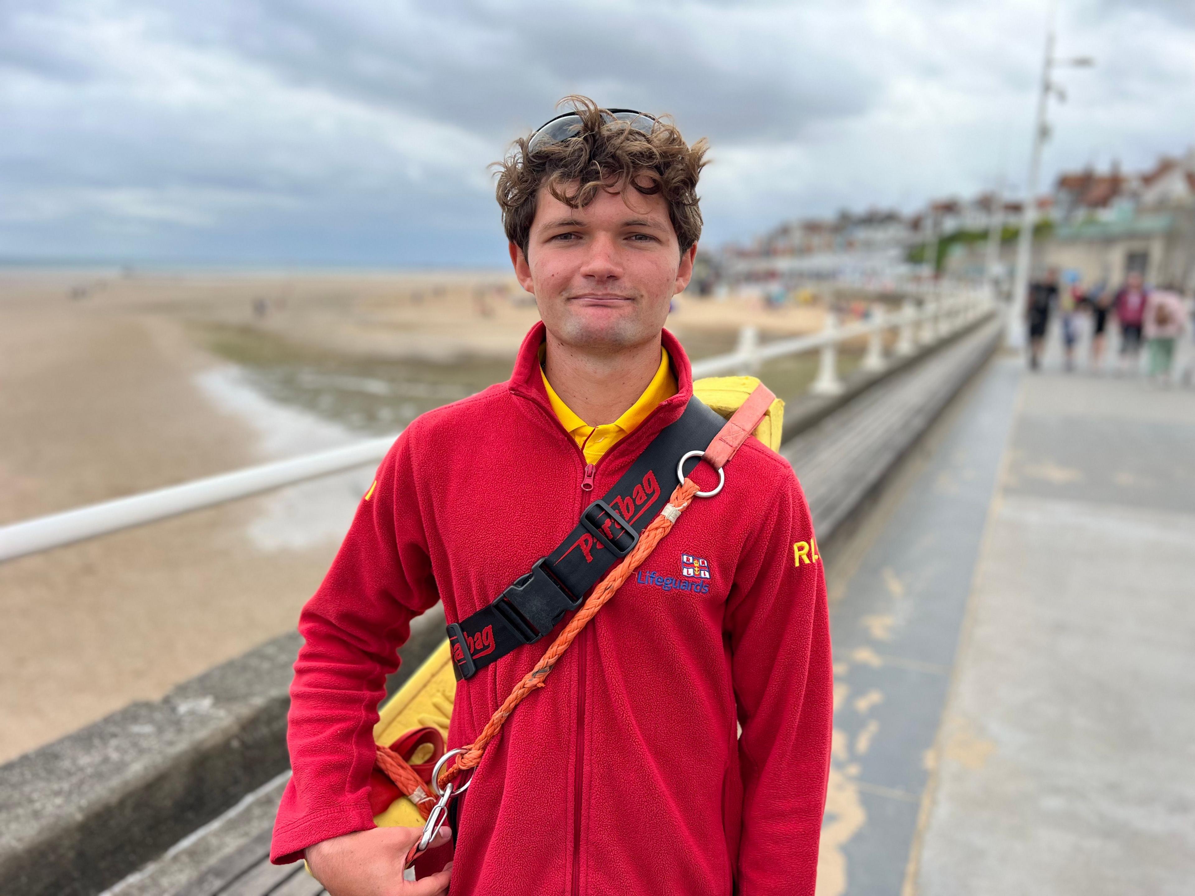 William Leggatt wearing his red RNLI uniform with a rescue float around his shoulder standing on Bridlington promenade