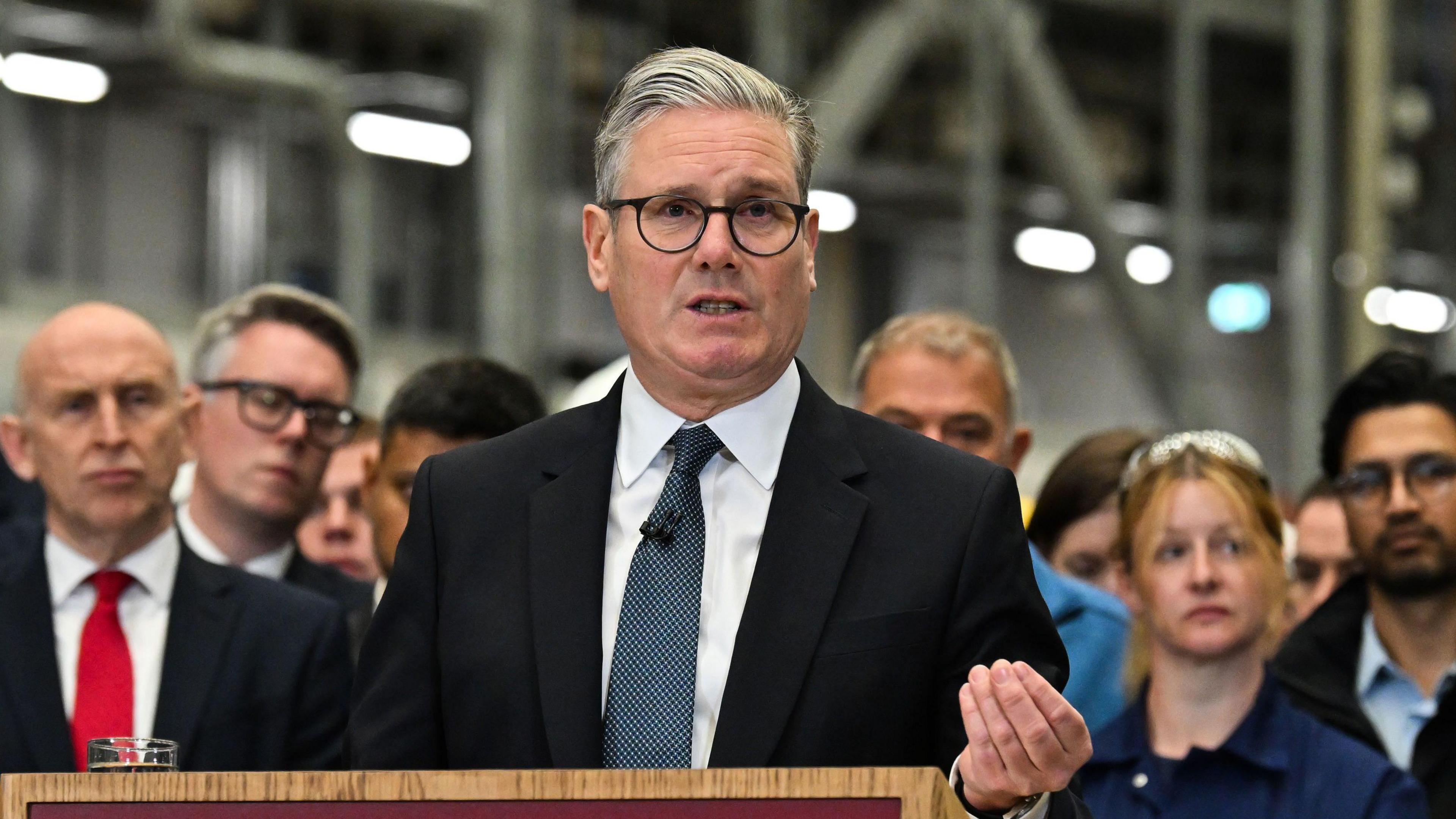 Sir Keir speaks from a podium. A group of people gather behind him.