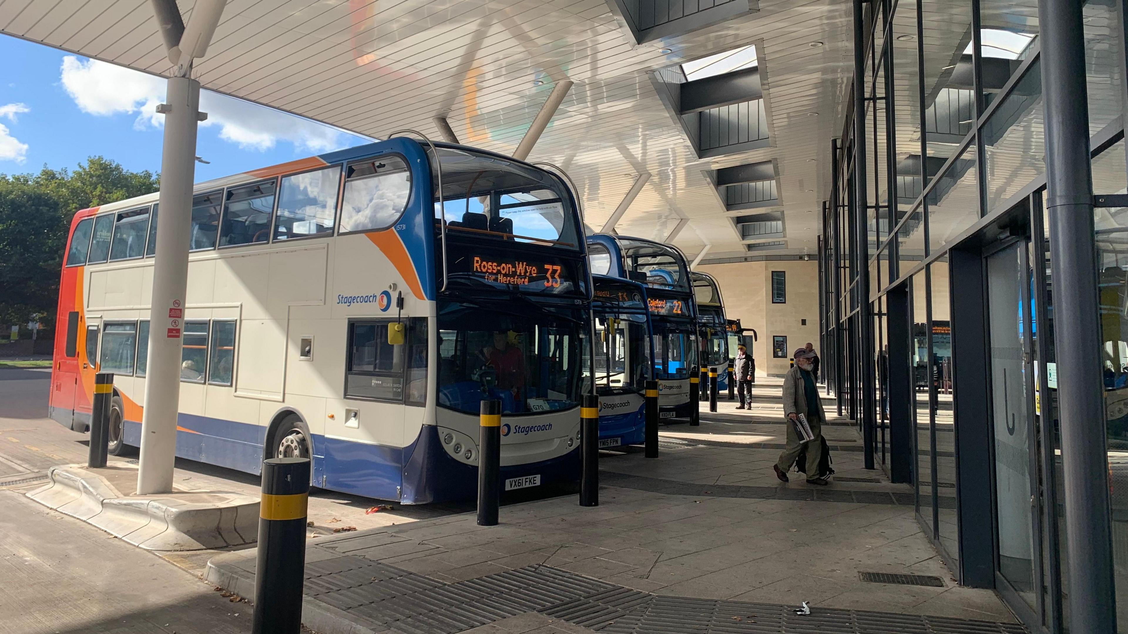 Buses lined up at a bus station under a roof.