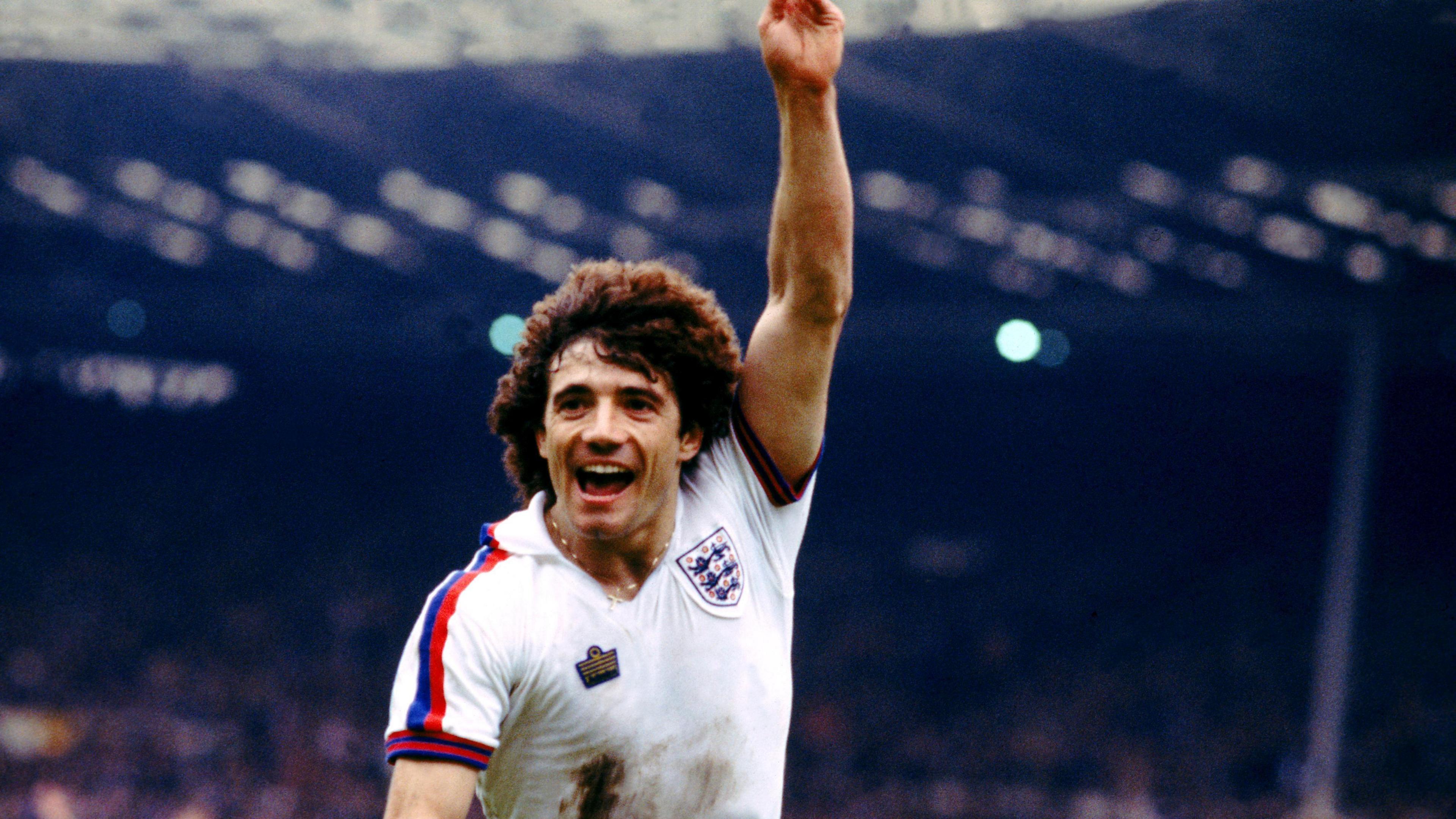 Kevin Keegan playing for England. He has one arm in the air and a big smile on his face.