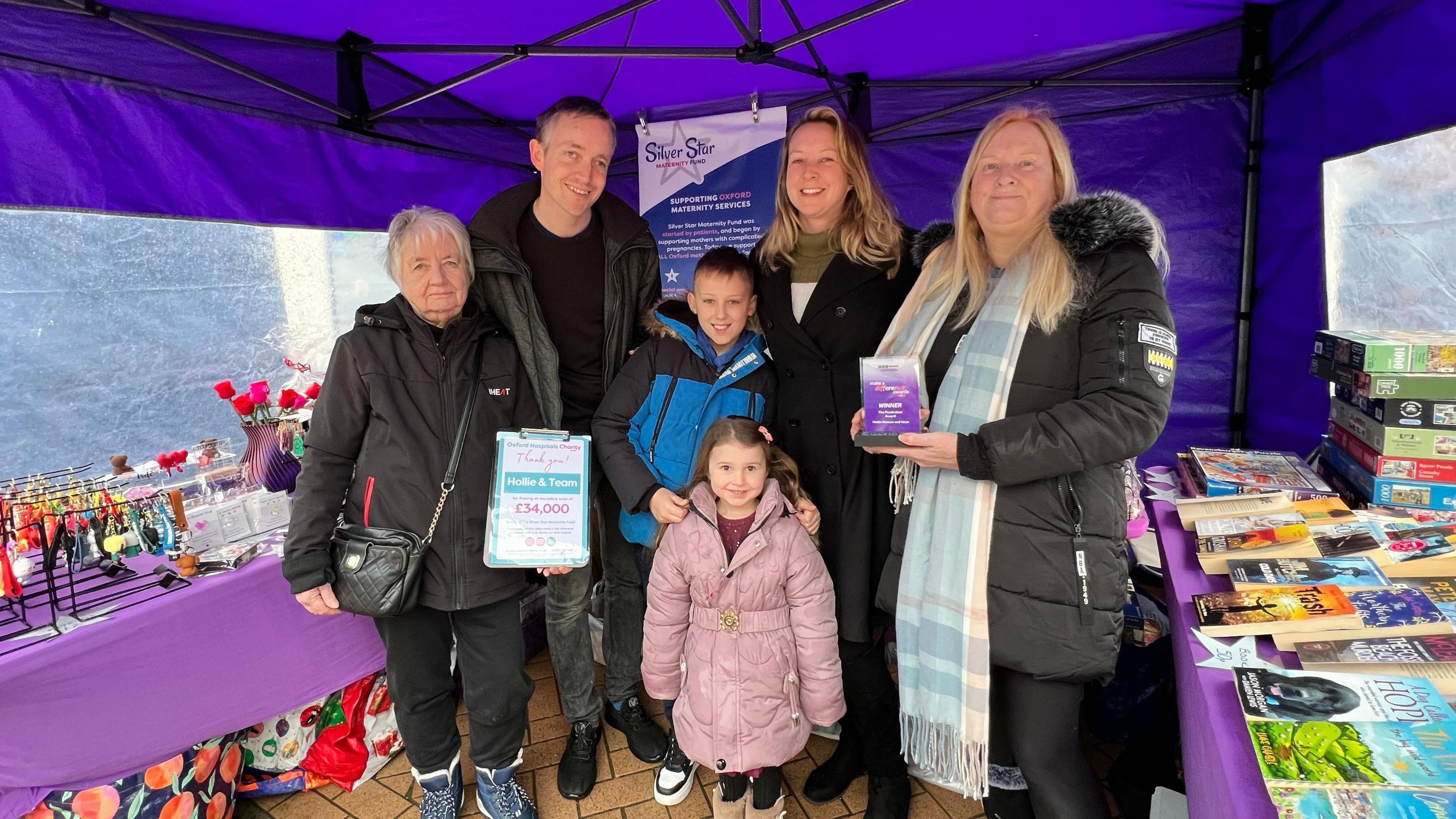 A group of people, three women and one man, along with one boy and one girl stood under a purple tent.