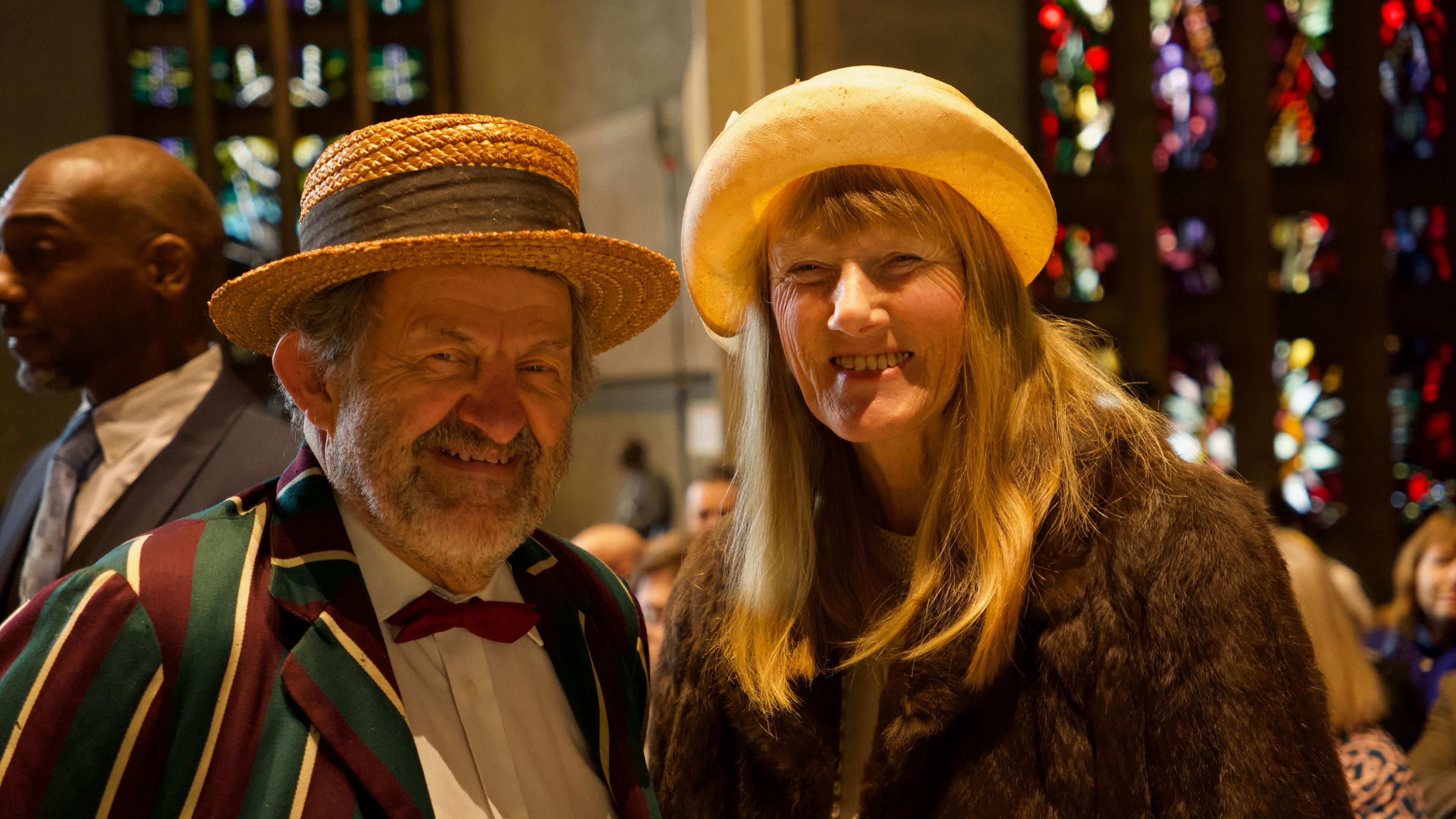 A man in a green and purple striped blazer and boater and a woman in a fur coat and hat