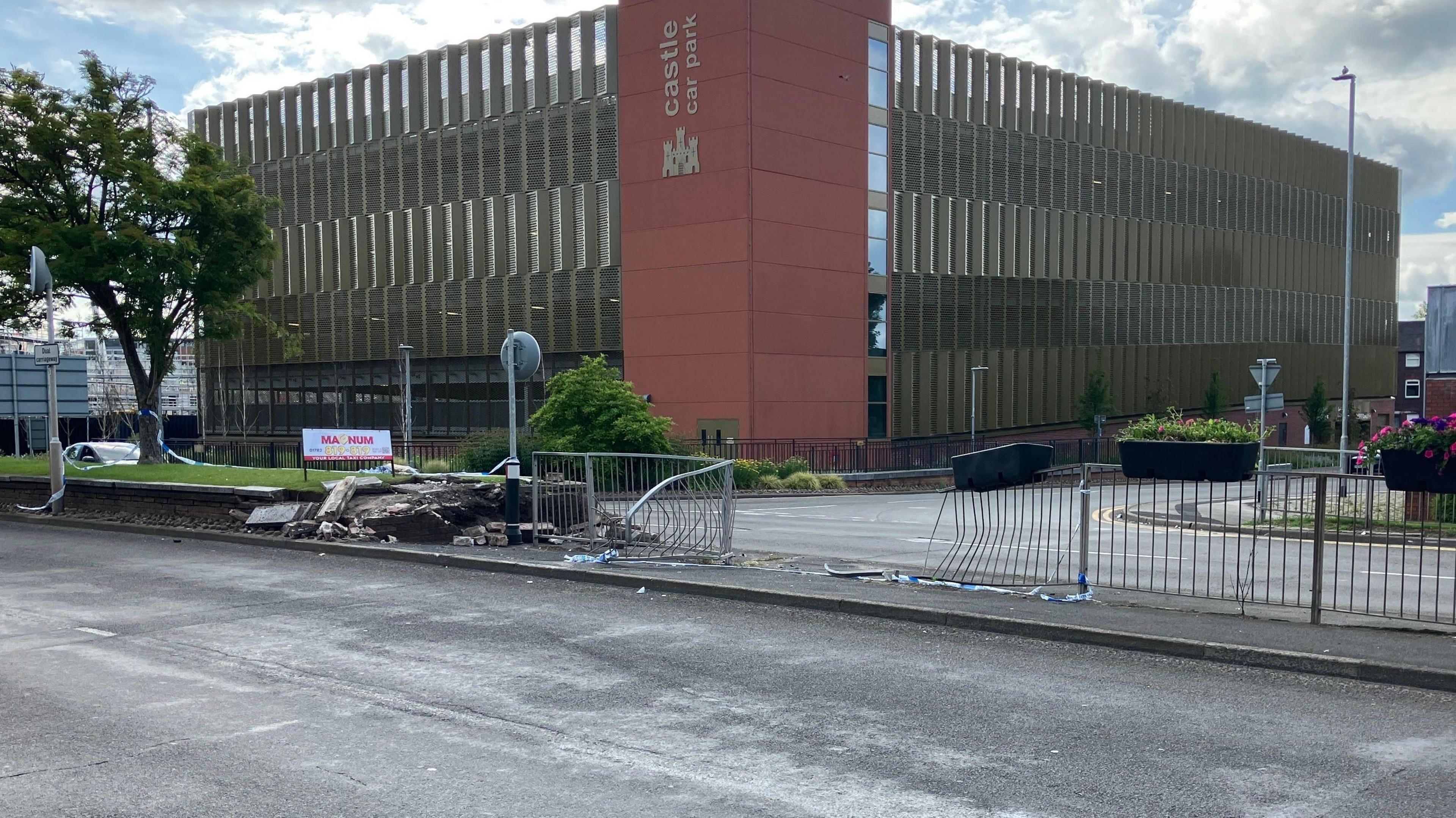 A street scene shows a damaged brick wall and police tape, suggesting a recent crash. A tree and the "Castle Car Park" can be seen in the background. 