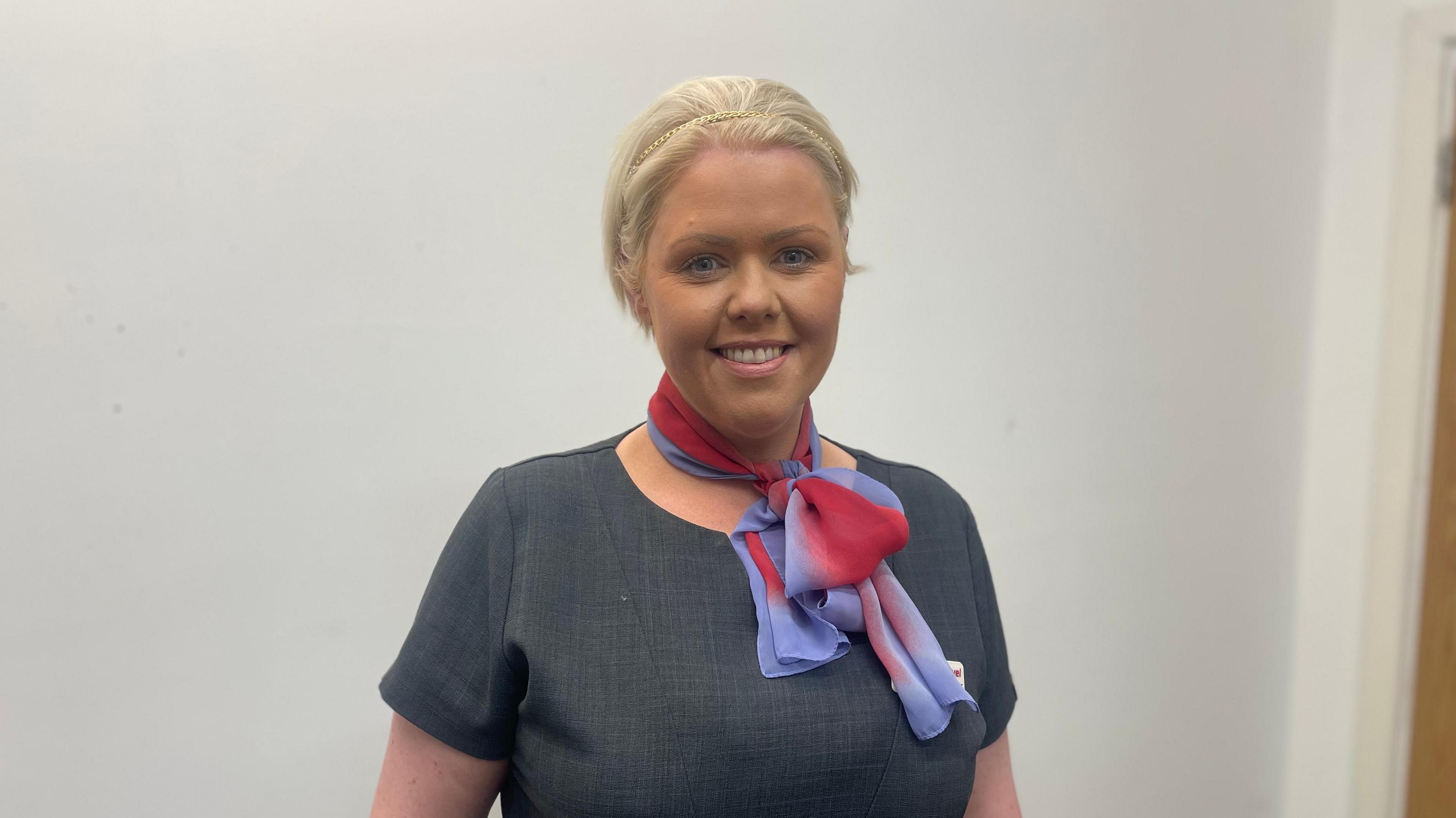 Katie Murray wearing a travel agents uniform smiling at camera with white background.