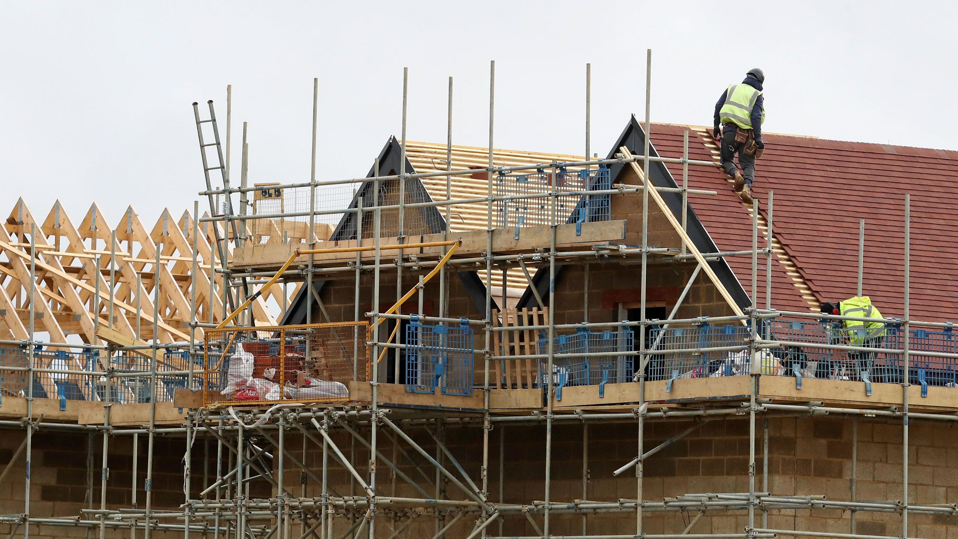A building site showing new homes being built. A workman can be seen standing on scaffolding.