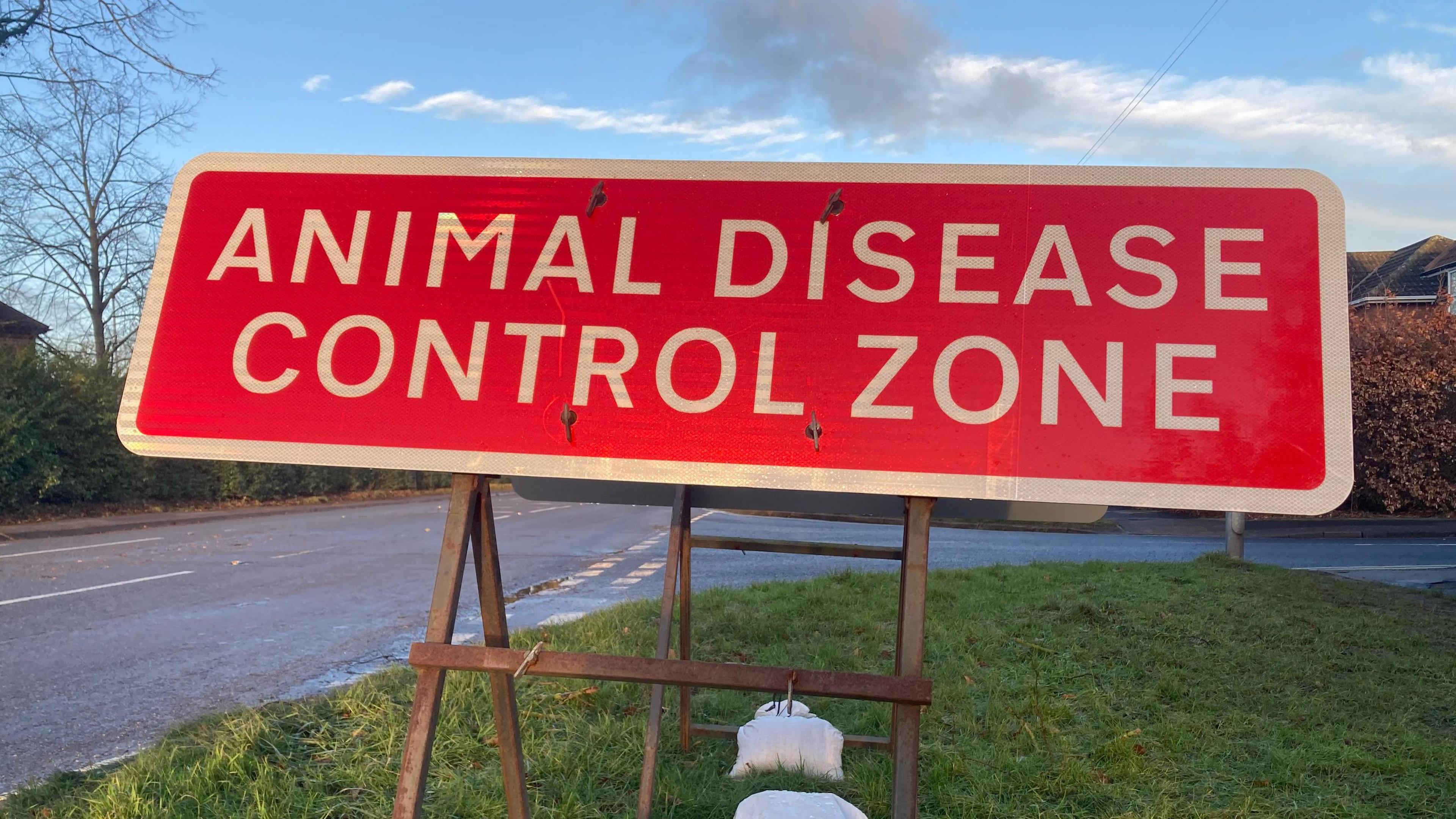 A red sign with white letters at the side of a road that says "animal disease control zone".