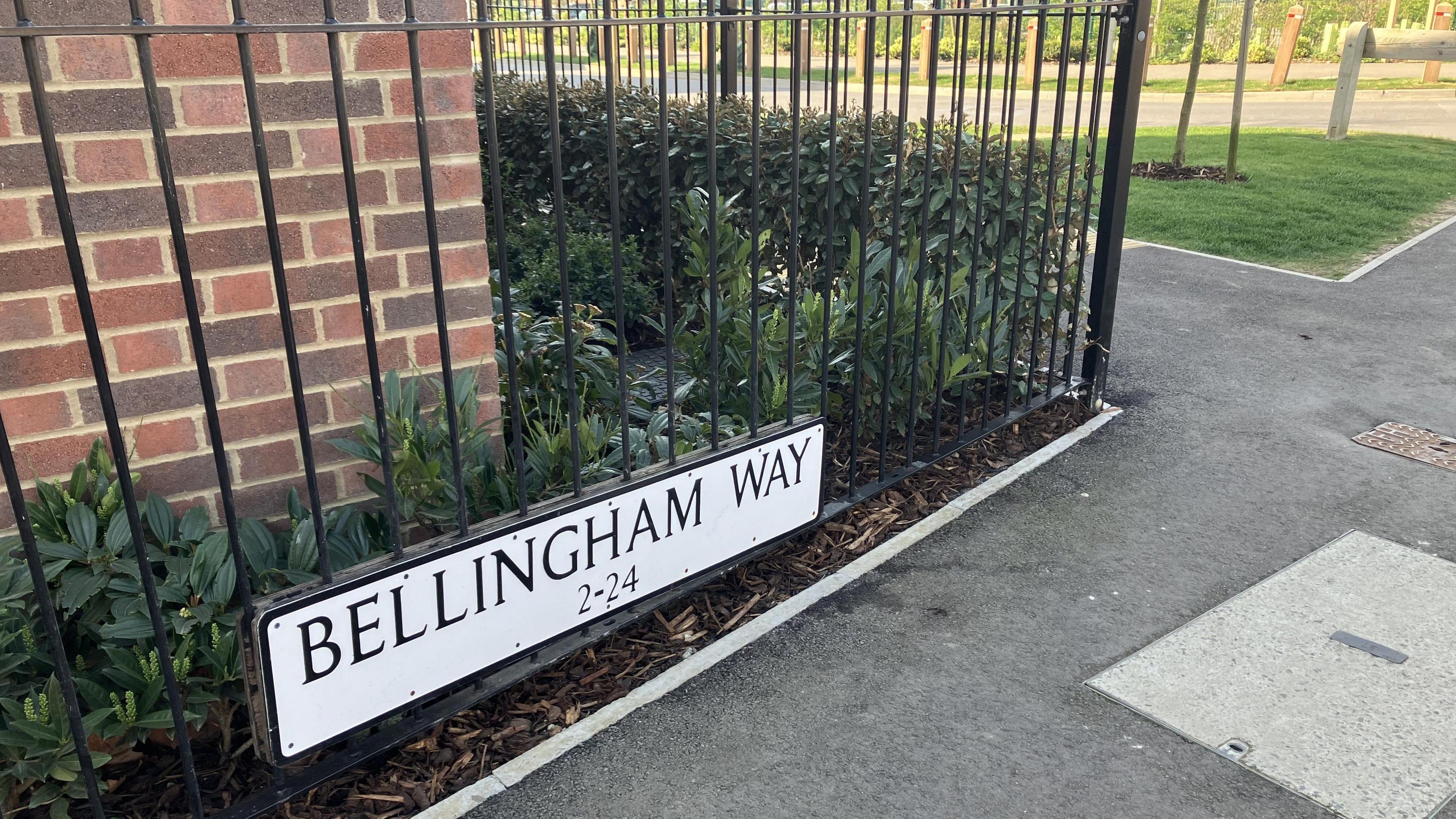 A picture of a road sign which says "Bellingham Way" on it - it is attached to iron railings next to a house.