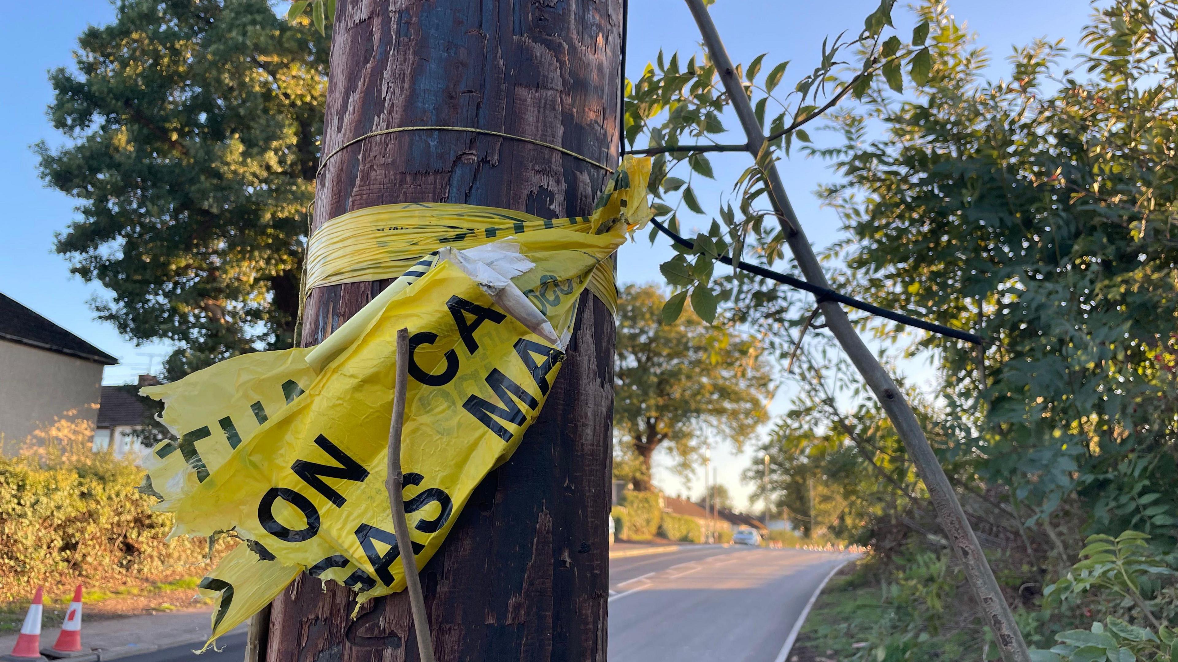A telegraph pole with a yellow "caution" ribbon wrapped around it